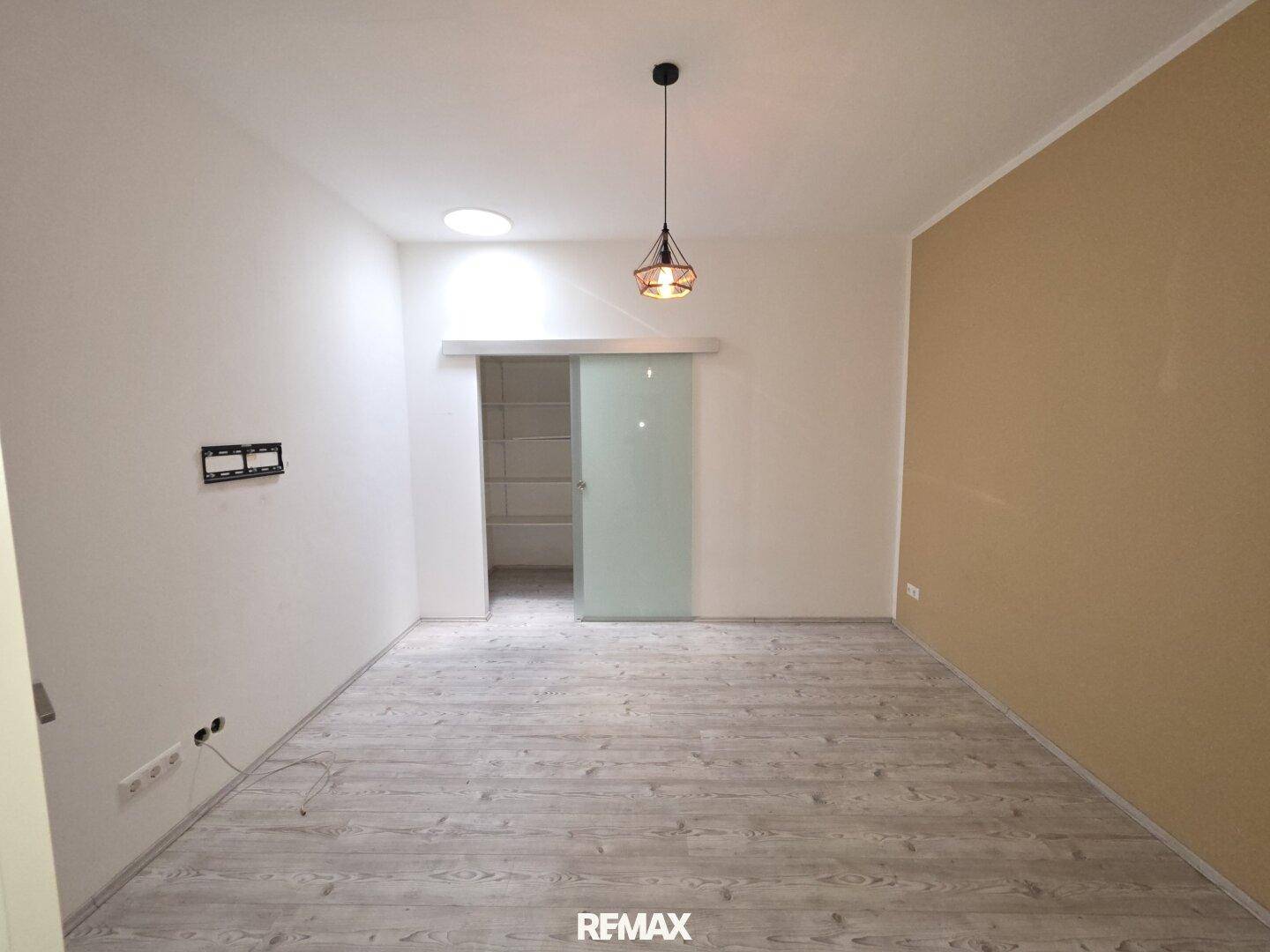 Helles Zimmer mit Laminatboden, Schiebetür zu einem begehbaren Schrank und Deckenlicht.
