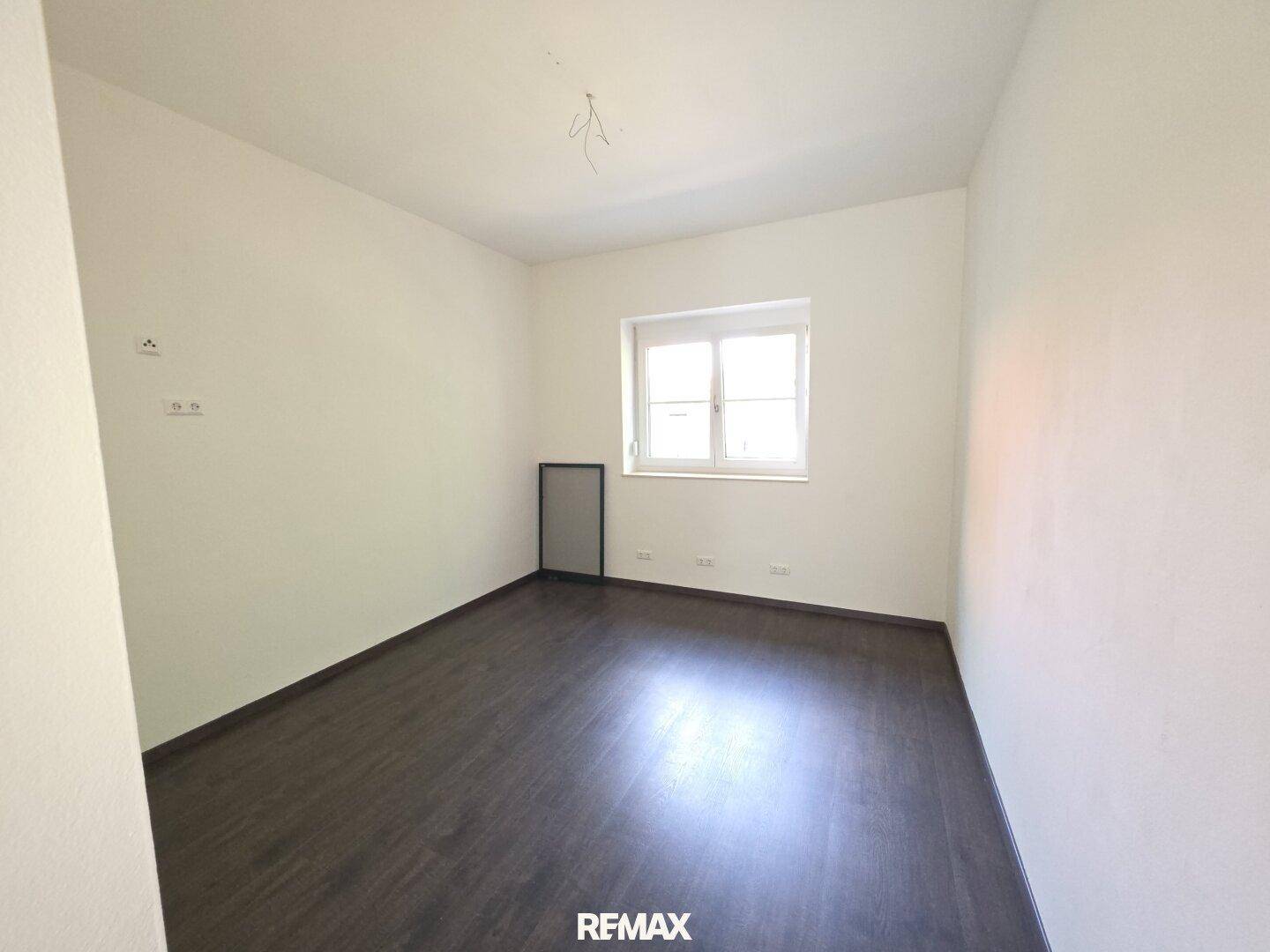 Ruhiges Schlafzimmer mit dunklem Laminatboden und einem Fenster für natürliches Licht.