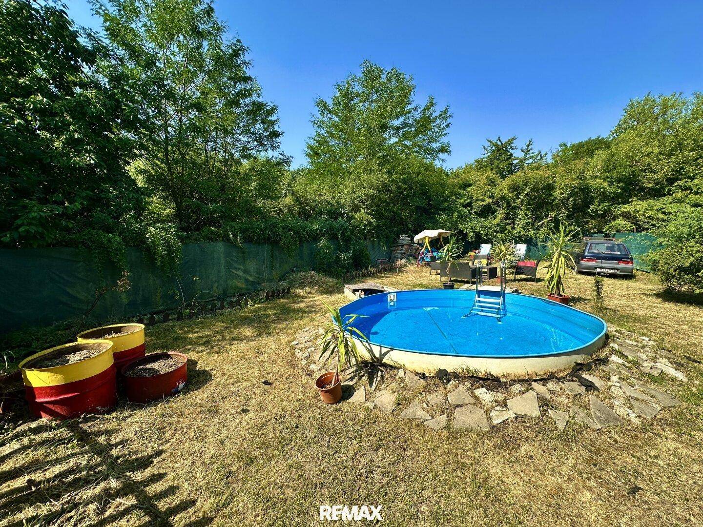 Großer Gartenbereich mit einem runden Aufstellpool, umgeben von viel Grün und Bäumen.