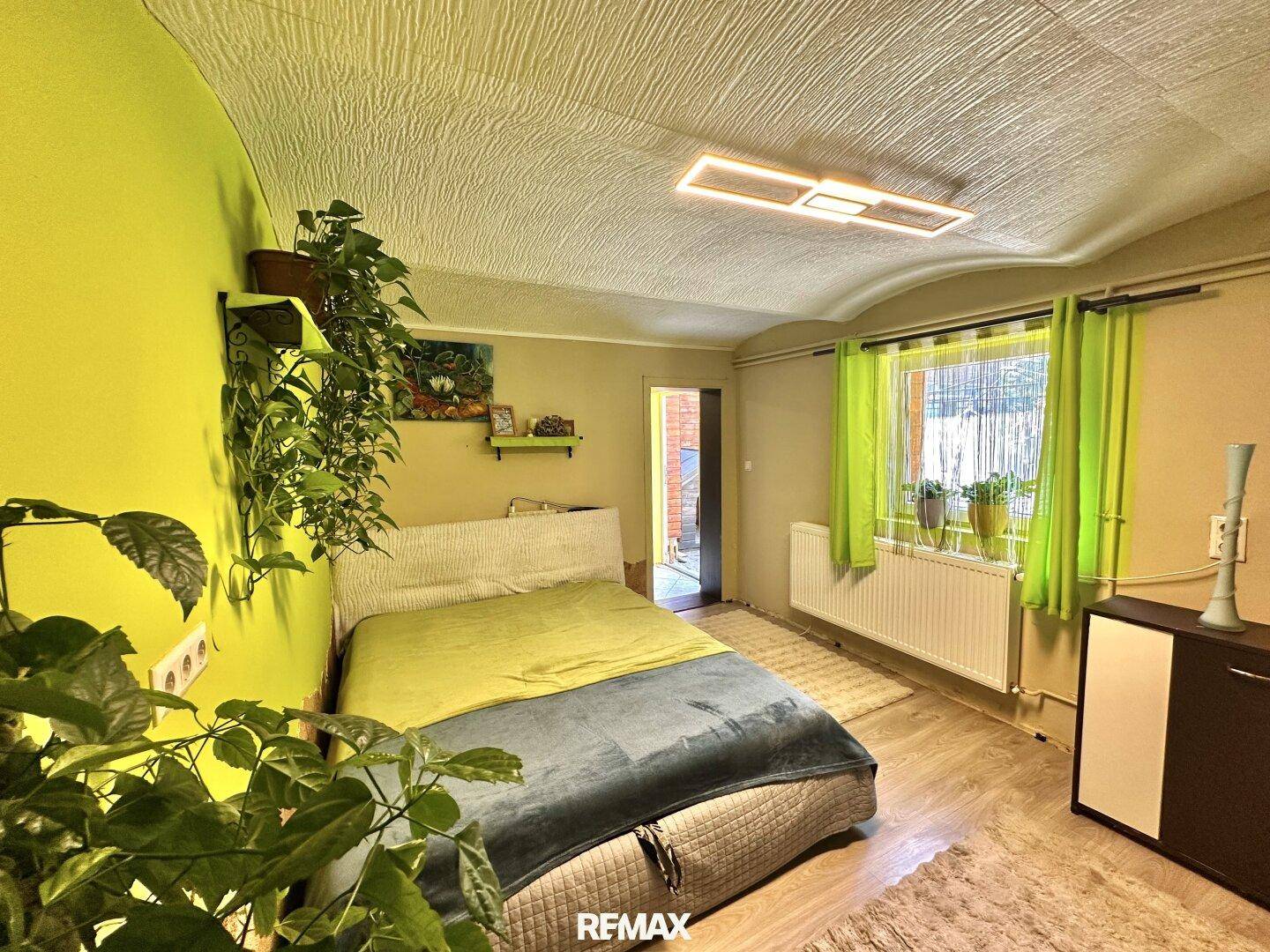 Schlafzimmer mit grün gestrichenen Wänden, Doppelbett und Laminatboden, hell und freundlich.