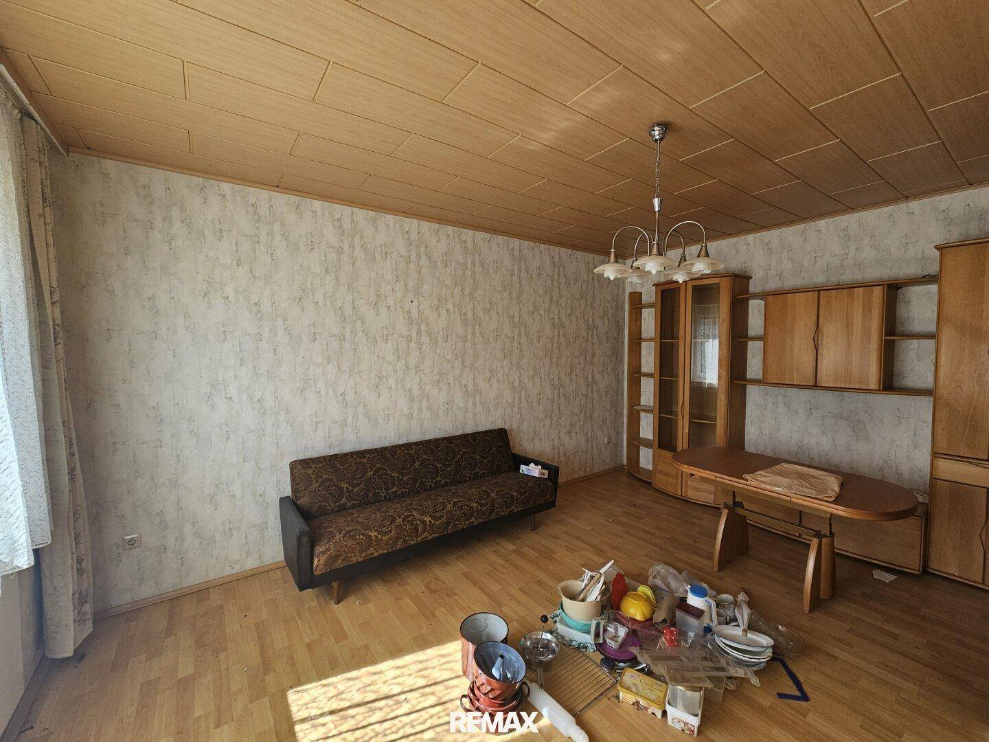 Geräumiges Wohnzimmer mit Holzdecke, älteren Möbeln und Tapeten, die eine Renovierung benötigen.