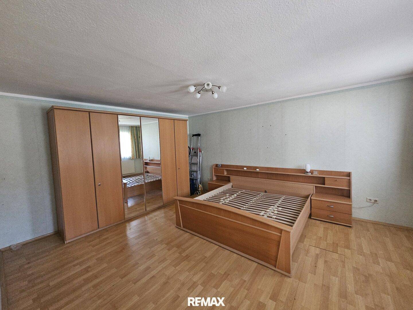 Schlafzimmer mit Holzbett und Kleiderschrank, Parkettboden und hellgrünen Wänden.