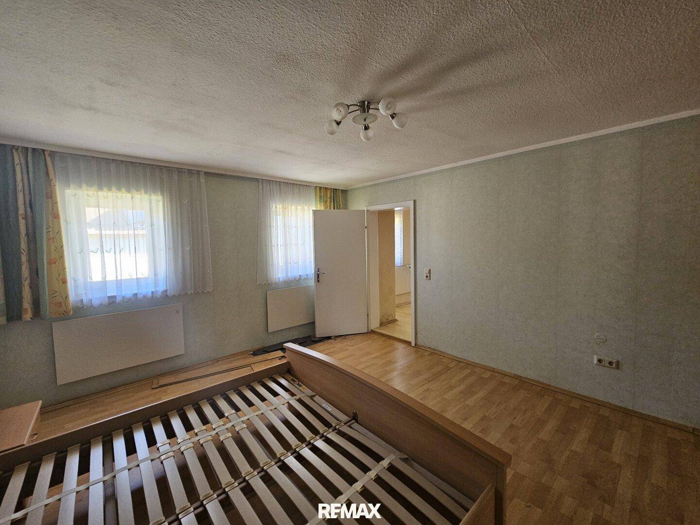 Schlafzimmer mit Parkettboden und zwei Fenstern, die viel Tageslicht hereinlassen.