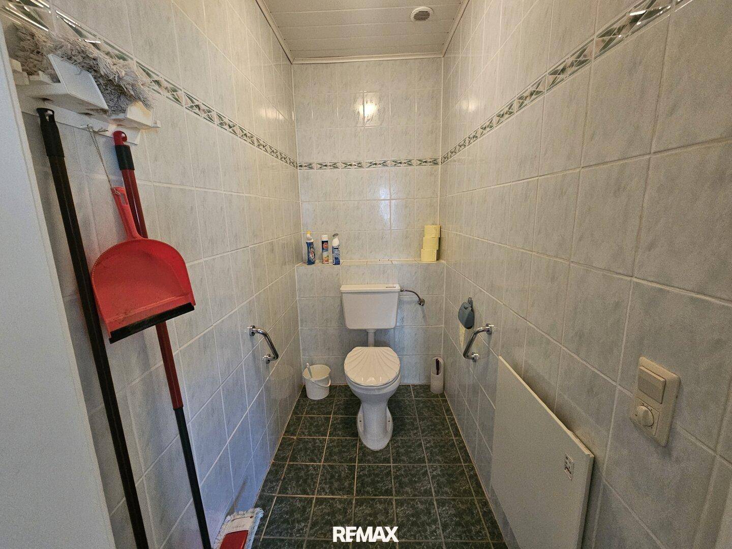 Separate Toilette mit Fliesen an Wänden und Boden, ausgestattet mit einem Heizkörper.