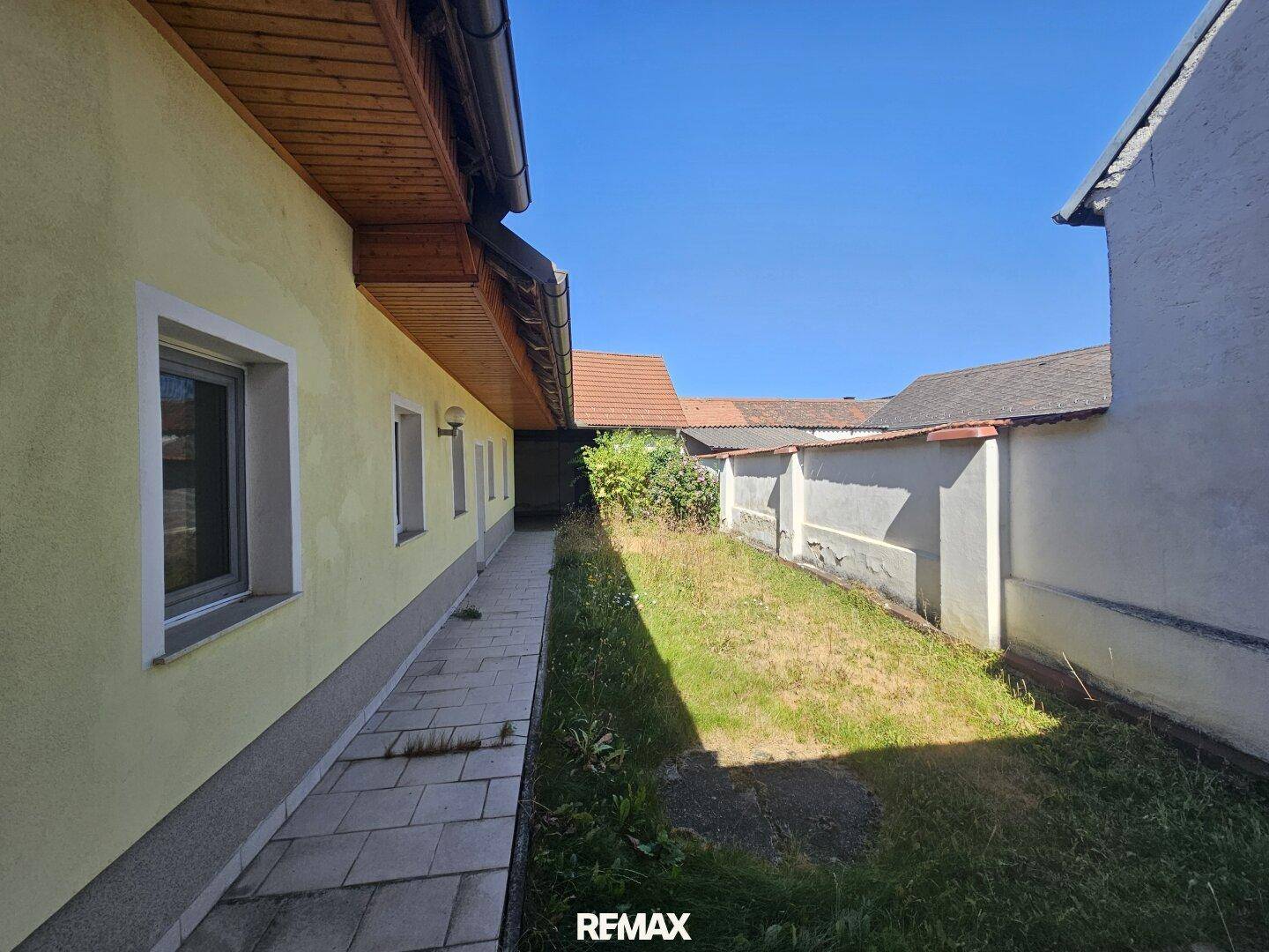 Seitenansicht des Hauses mit einem gepflasterten Weg und einem schmalen Gartenbereich.