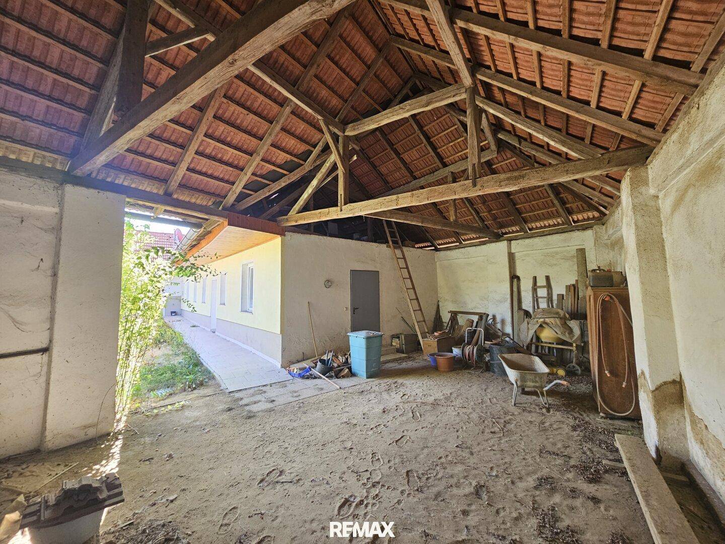 Offene Scheune mit Holzdachkonstruktion und Blick auf das angrenzende Gebäude.