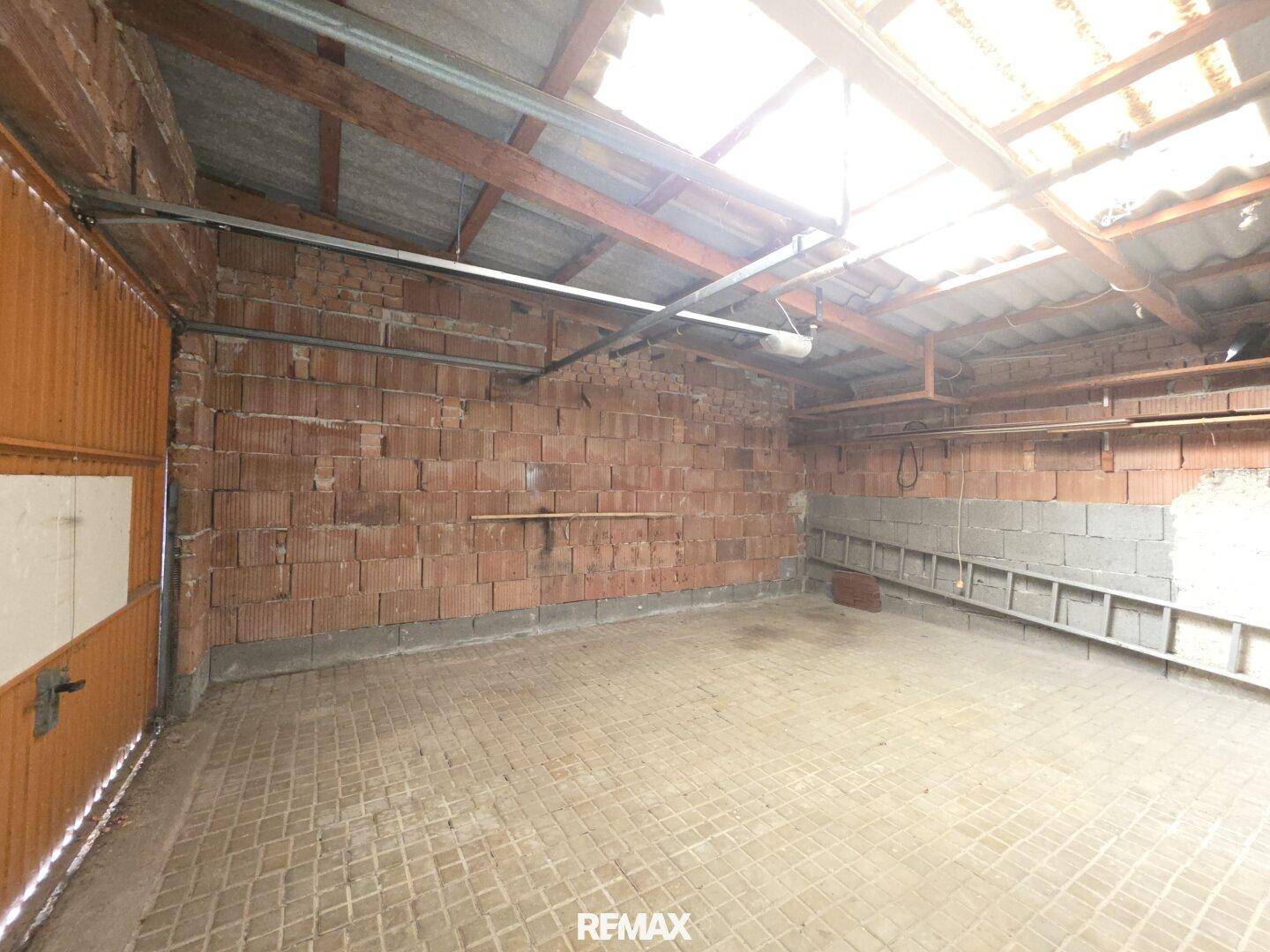 Geräumige Garage mit Ziegelwänden, Betonboden und sichtbarer Dachkonstruktion.