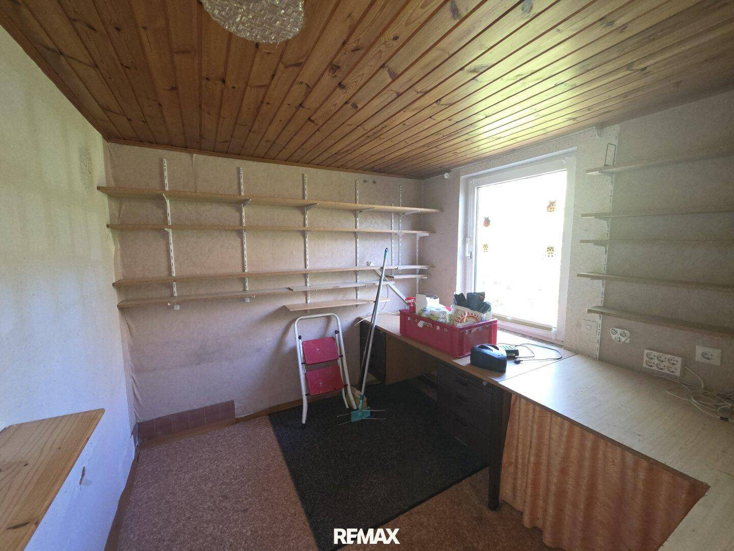 Arbeitszimmer mit Holzdecke, Regalen an den Wänden und einem Schreibtisch am Fenster.