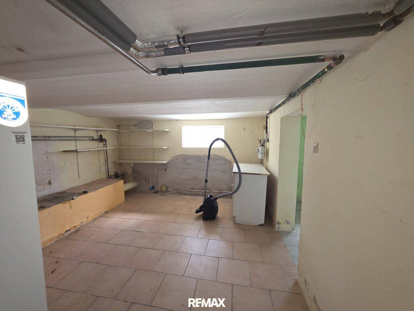 Hauswirtschaftsraum im Keller mit Fliesenboden, Waschbecken und sichtbaren Rohren.