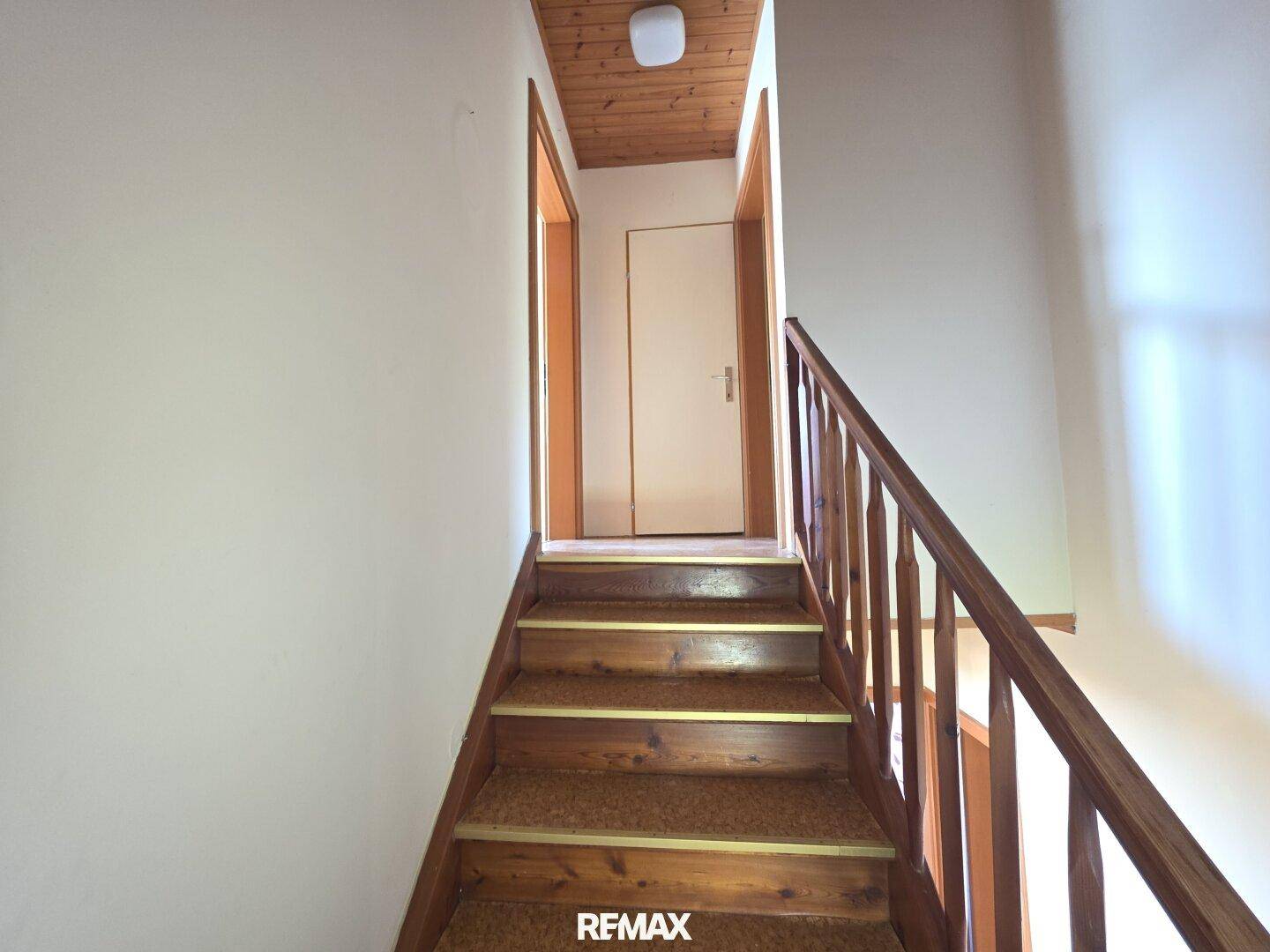 Holztreppe mit Teppichstufen und Holzgeländer führt zu den Zimmern im Obergeschoss.