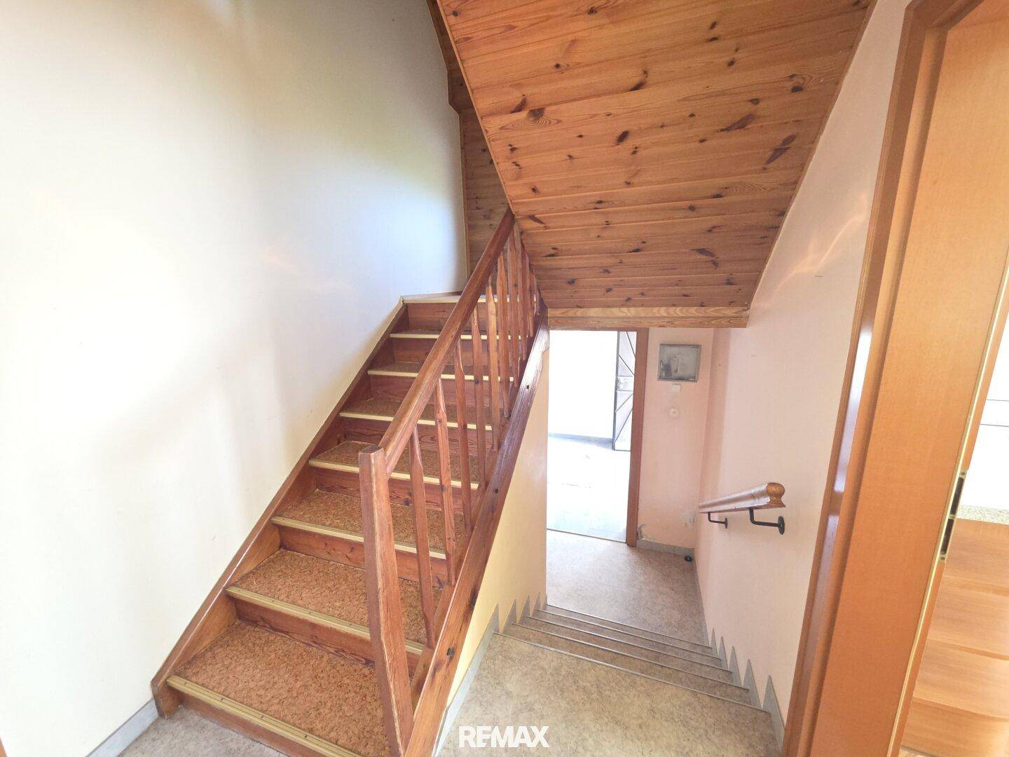 Holztreppe mit Teppichstufen und Holzgeländer führt in das obere Stockwerk.