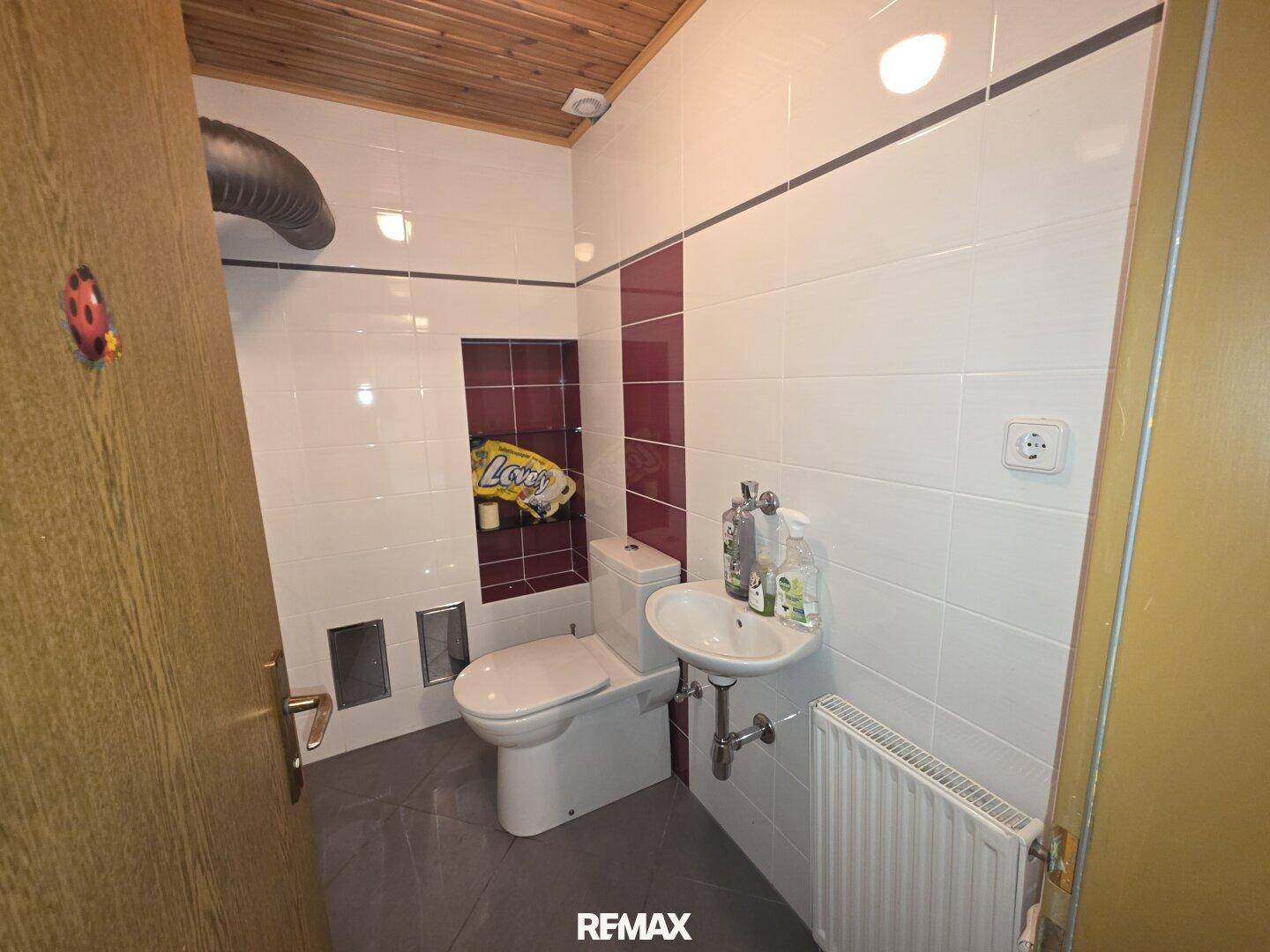 Kleines WC mit weißen Fliesen, Waschbecken und Heizkörper unter einer Holzdecke.