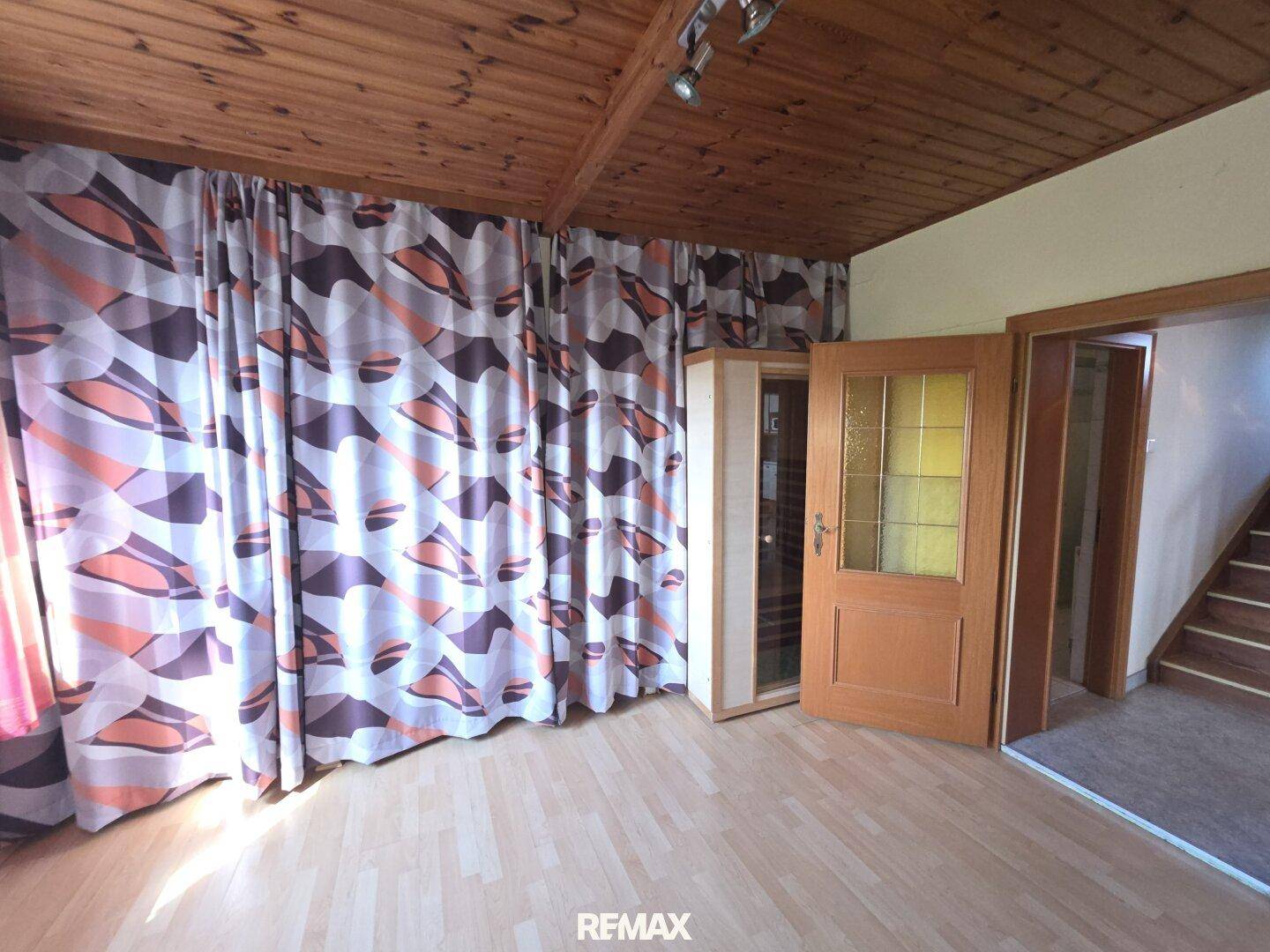 Schlafzimmer mit Holzboden, gemusterter Vorhangwand und Zugang zu einer Treppe.