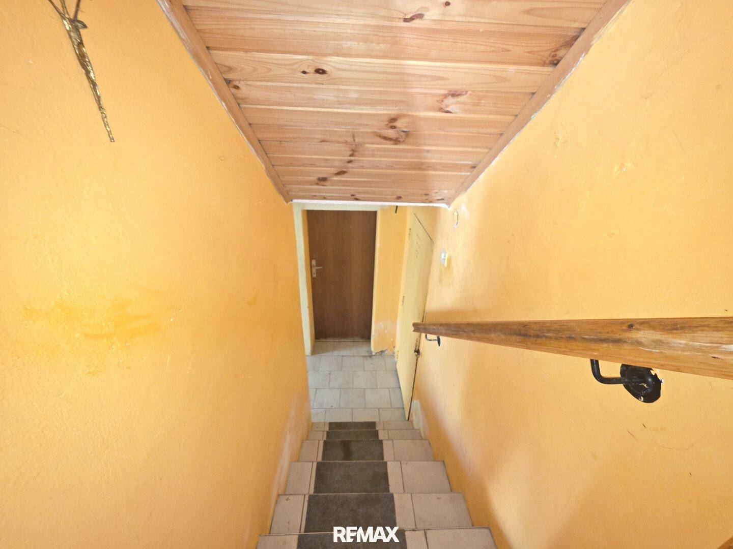 Treppe führt in den Kellerbereich mit gelb gestrichenen Wänden und Holzdecke.