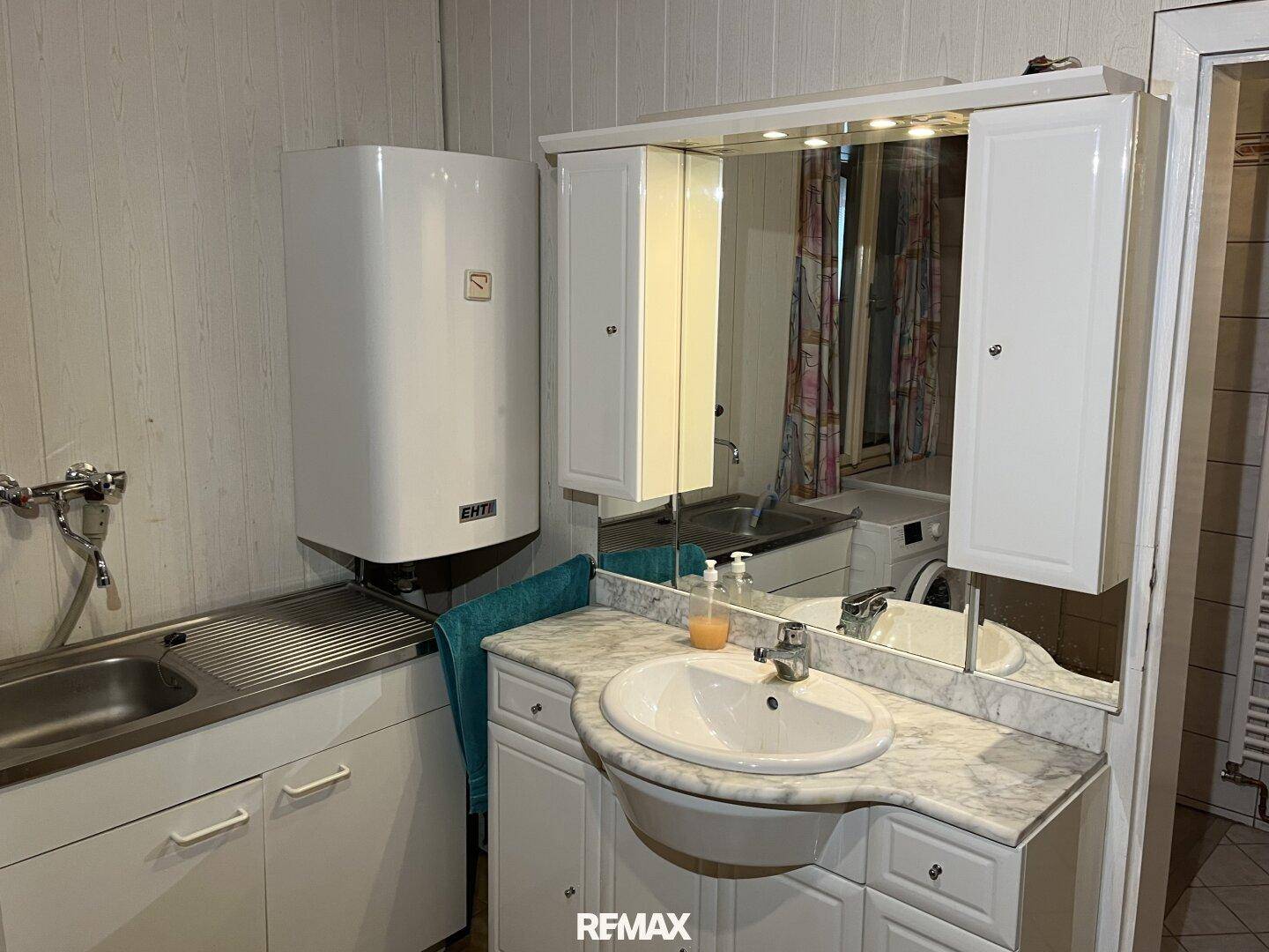 Badezimmer mit Waschbecken, Spiegelschrank, Warmwasserboiler und Waschmaschine.