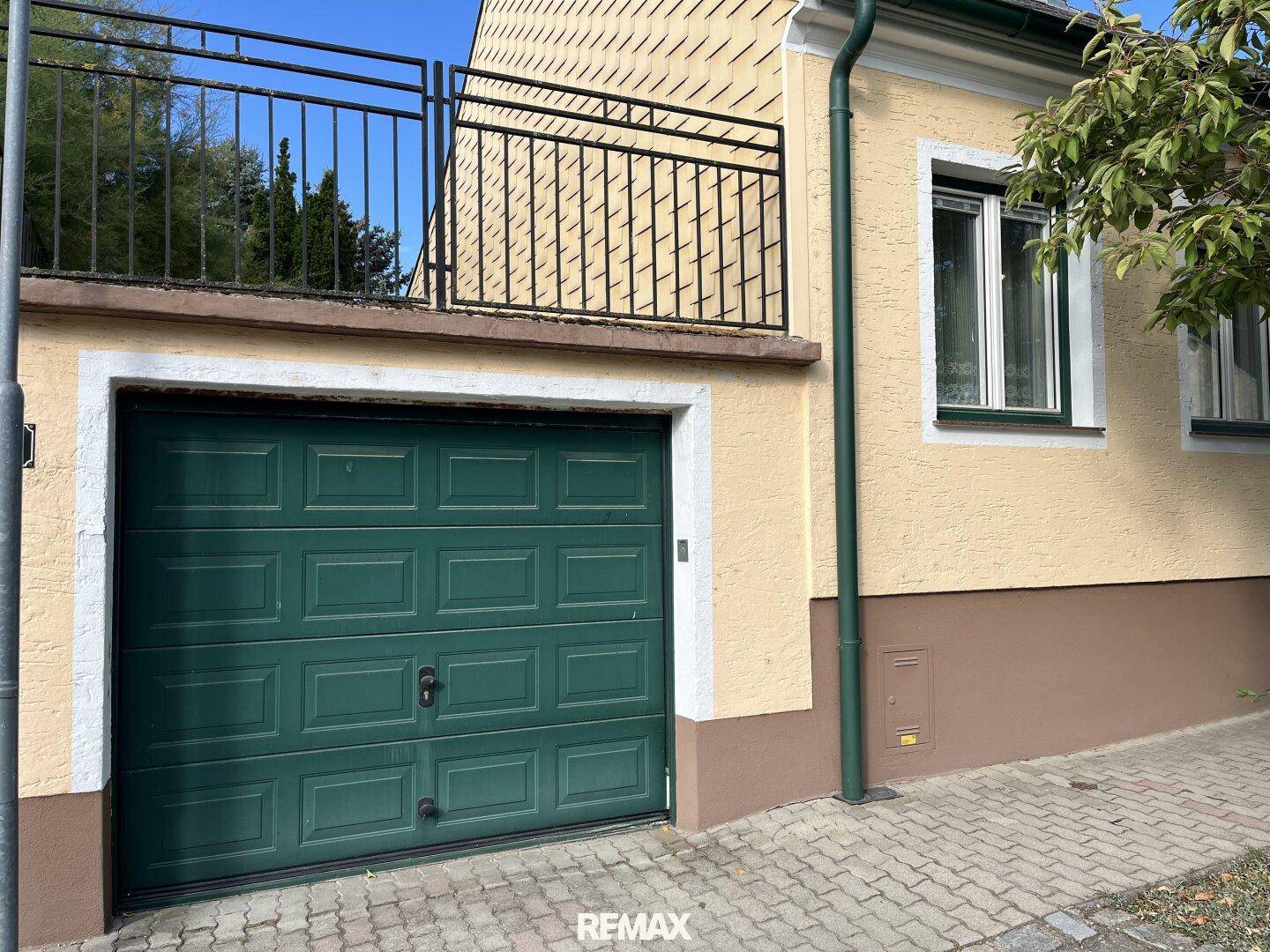 Grüne Garagentür an der Hausfassade mit einem kleinen Balkon oder einer Terrasse darüber.