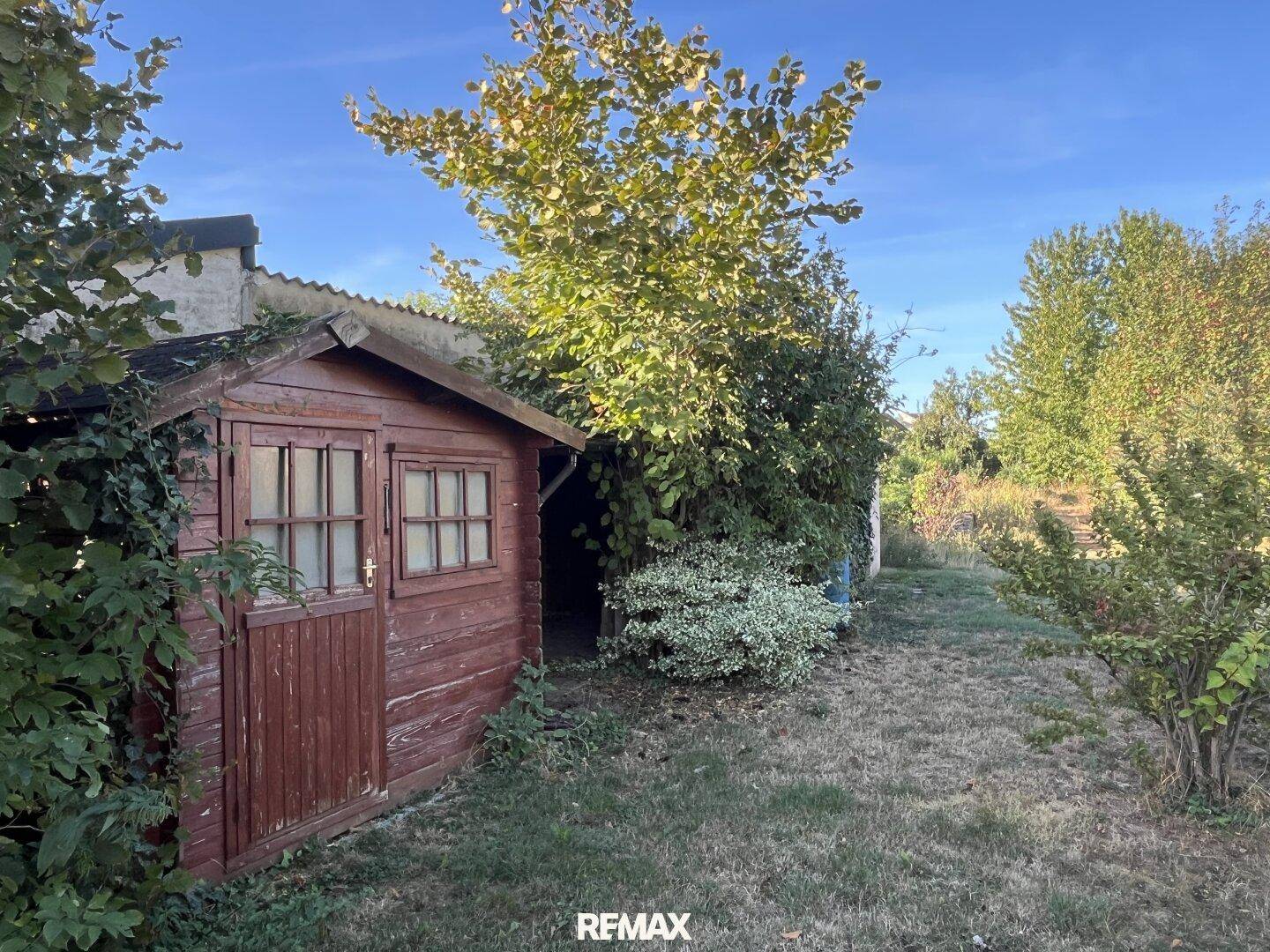 Kleiner hölzerner Gartenschuppen in einer grünen Umgebung mit Bäumen.