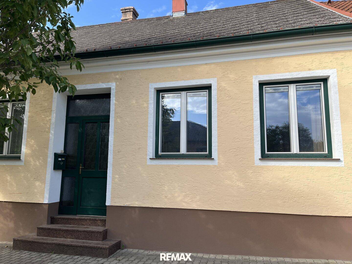 Eingangsbereich des Hauses mit grüner Tür, Fenstern und Steinstufen.