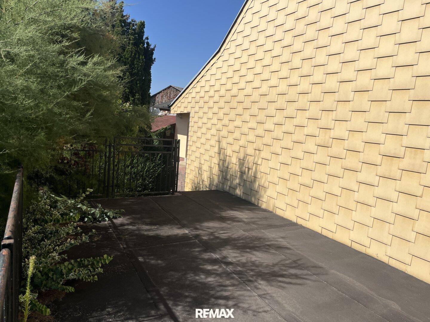 Flachdachbereich neben einer Hauswand mit gelben Schindeln unter blauem Himmel.