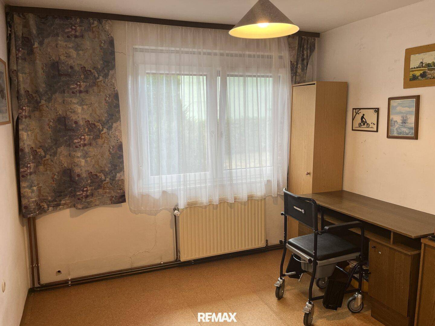 Schlafzimmer oder Arbeitszimmer mit Fenster, Heizkörper und einfacher Einrichtung.