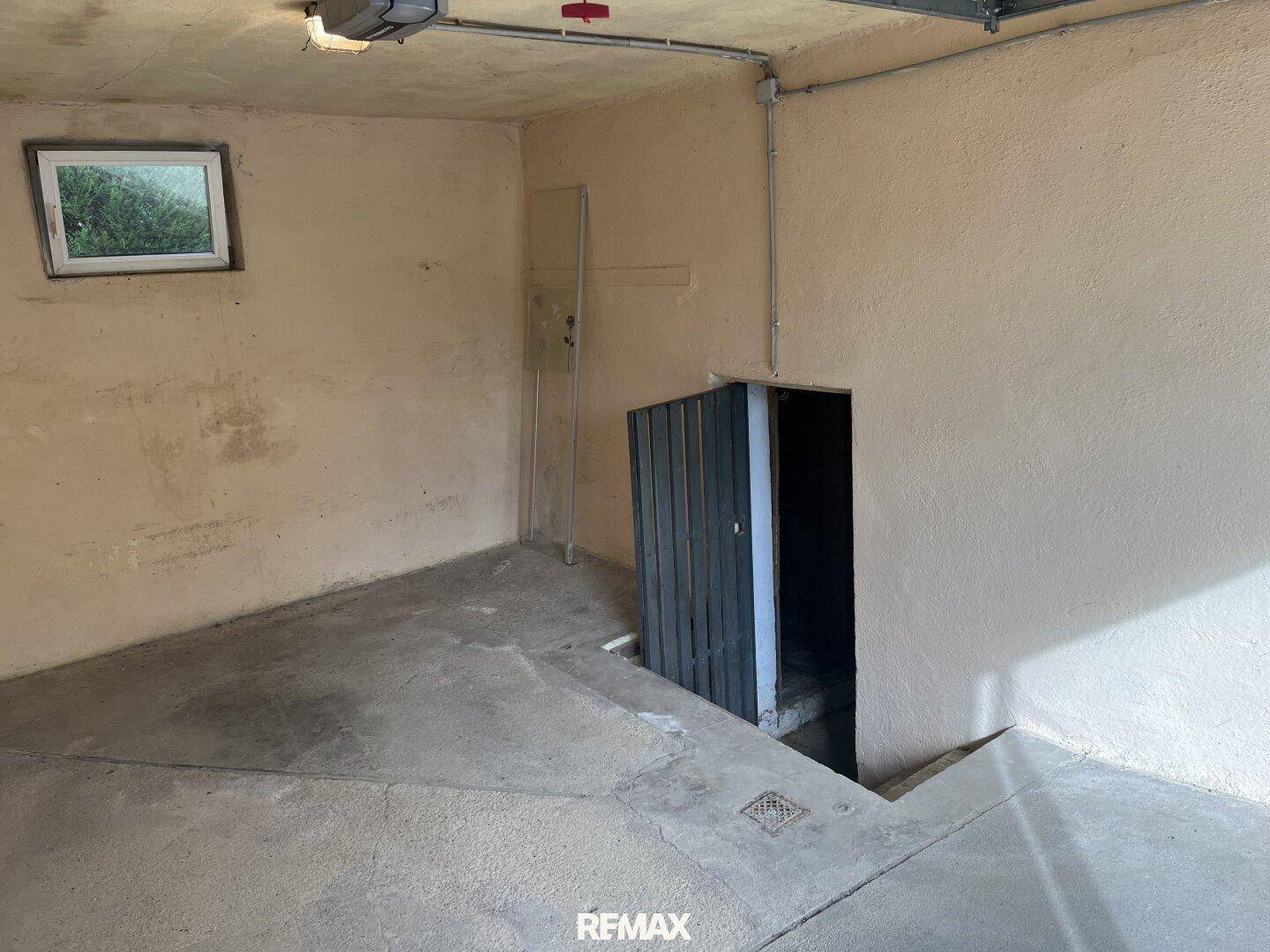 Geräumige Garage mit Betonboden und Zugang zu einem Kellerbereich.