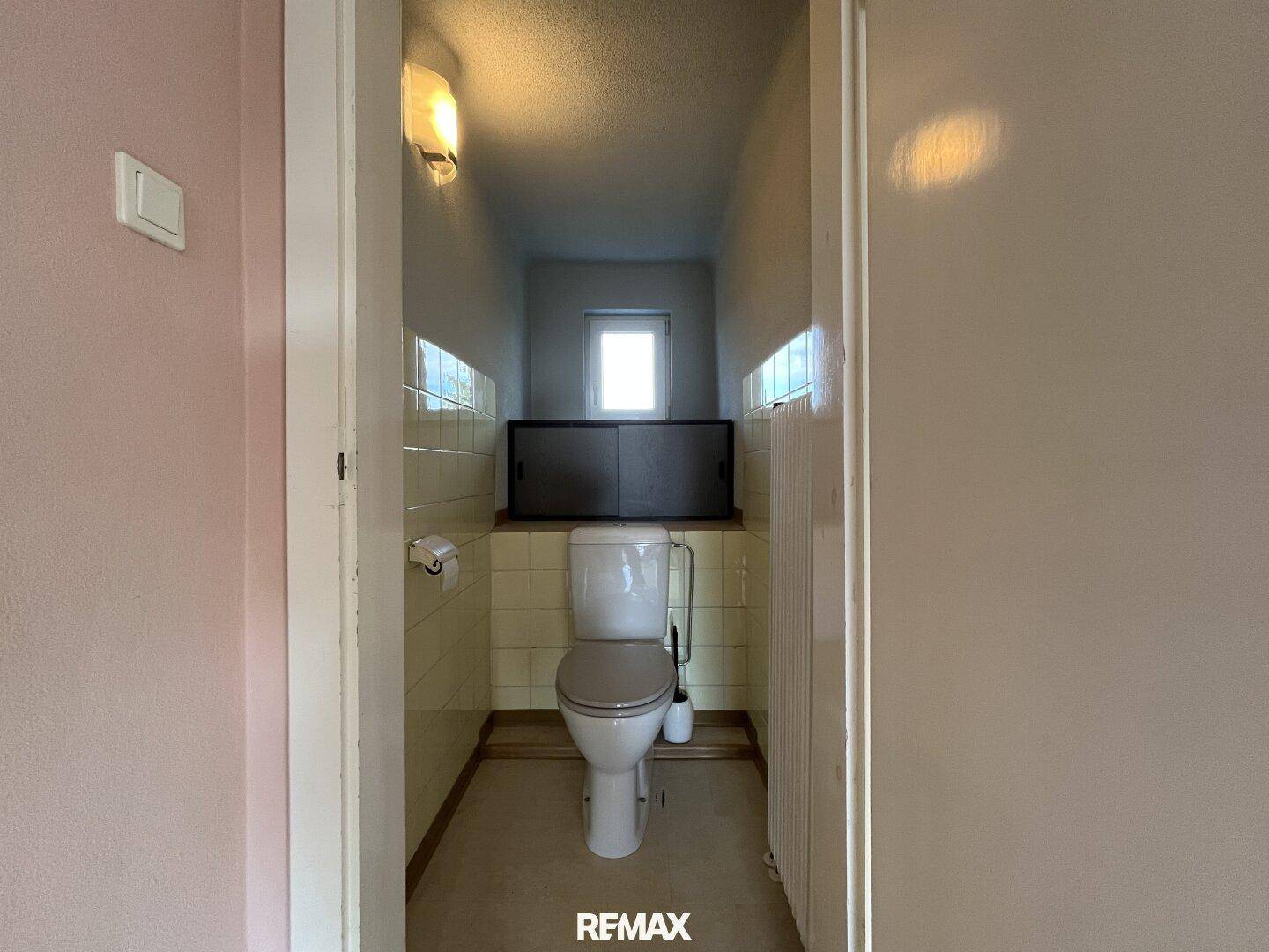 Kleines Gäste-WC mit Fenster, WC und hellen Fliesen an den Wänden.