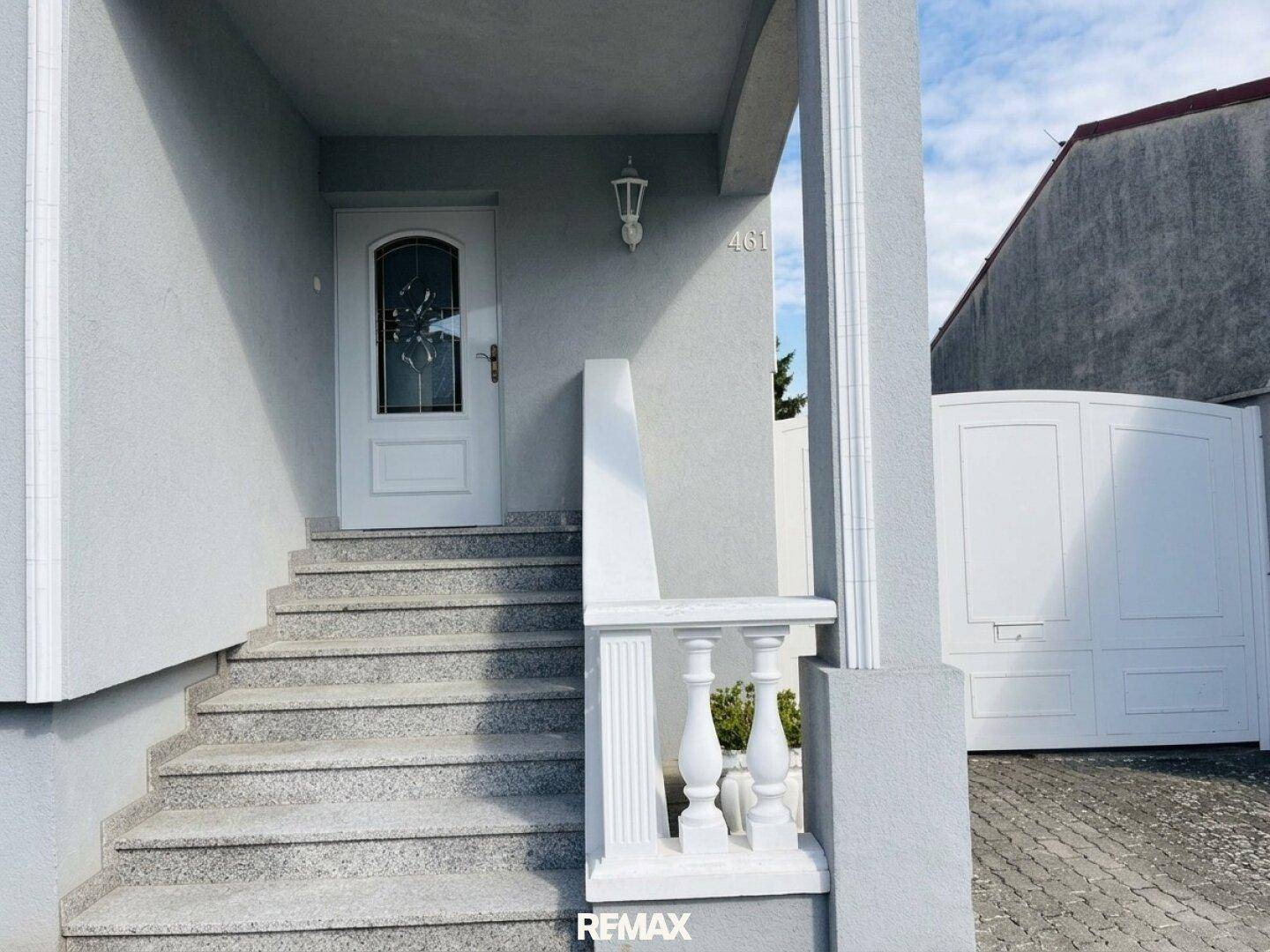 Eingangsbereich des Hauses mit Granittreppe, weißer Tür und dekorativem Geländer.
