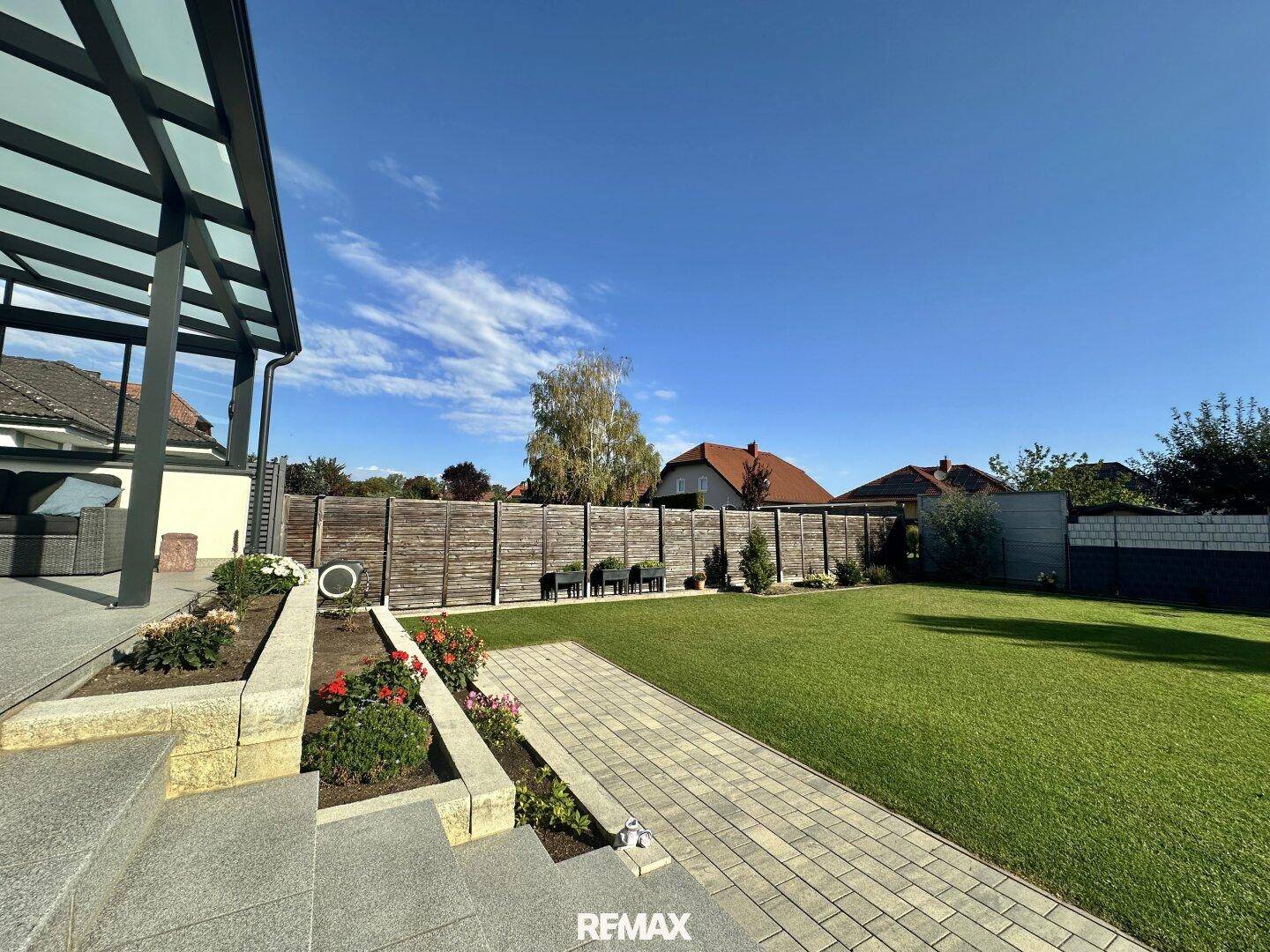 Gepflegter Garten mit Rasenfläche, Blumenbeeten und einem Weg, der zum Haus führt.