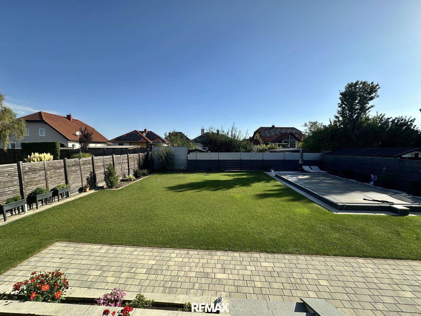 Weitläufiger Garten mit großem Rasenbereich und einem abgedeckten Swimmingpool unter blauem Himmel.