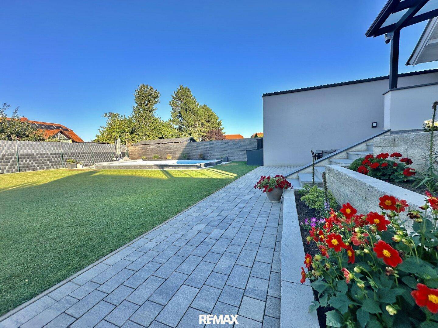 Langer Weg durch den grünen Garten, gesäumt von Blumen, führt zum Poolbereich im Hintergrund.