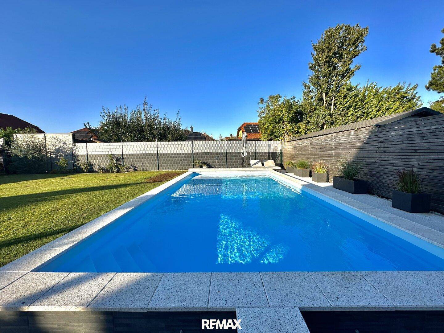 Großer, sauberer Swimmingpool mit hellen Fliesenrändern, umgeben von einer gepflegten Rasenfläche.