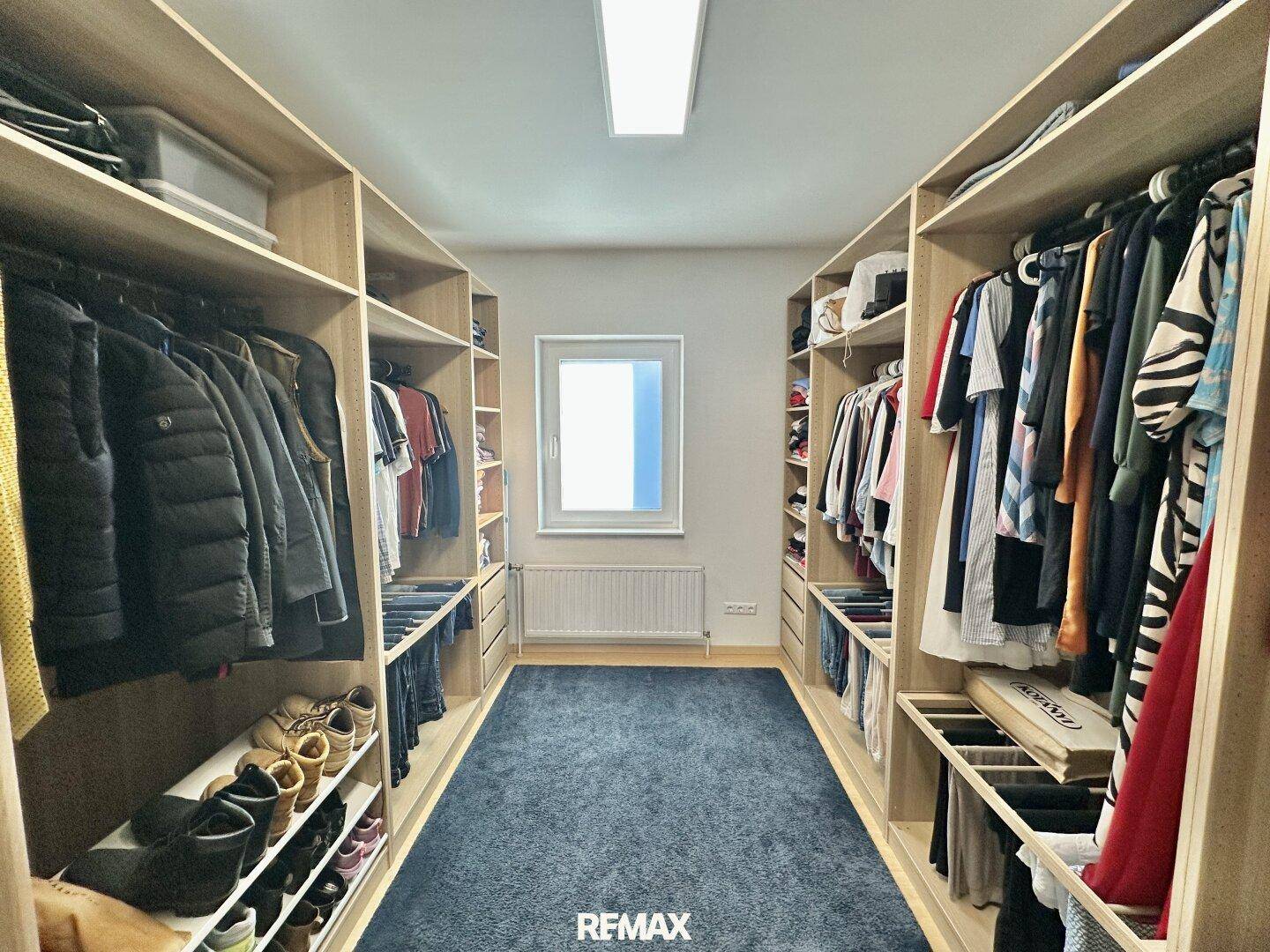 Geräumiger begehbarer Kleiderschrank mit viel Stauraum, Regalen und einem Fenster für Tageslicht.