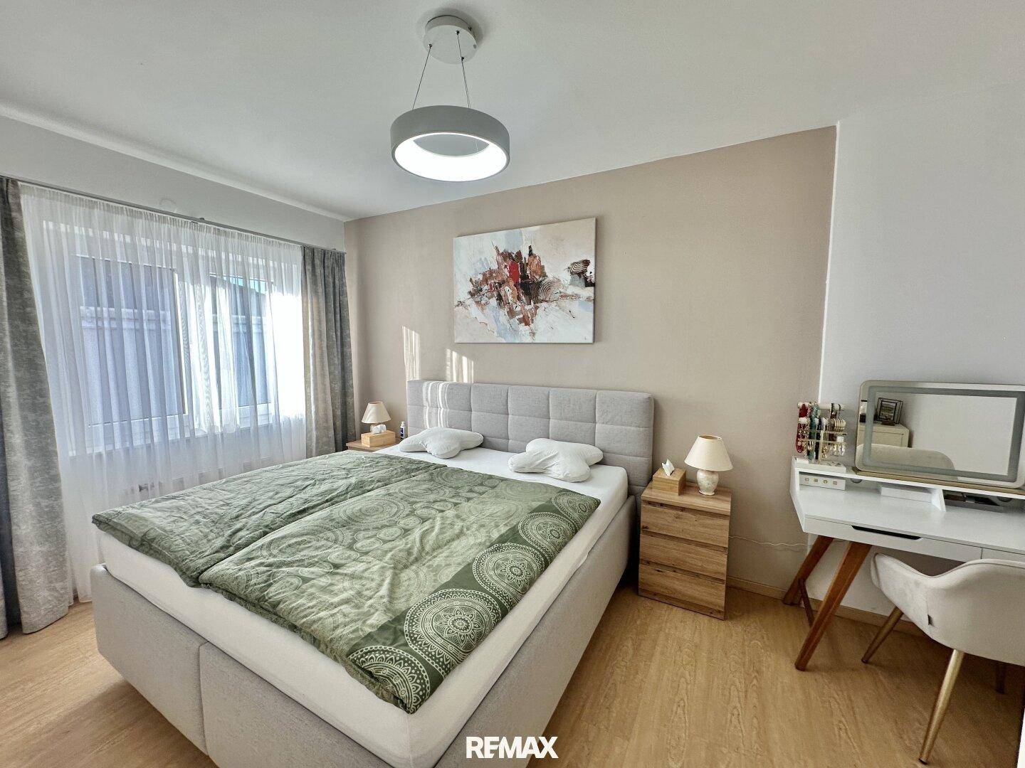 Modernes Schlafzimmer mit Doppelbett, Nachttischen und einem Schminktisch unter dem Fenster.