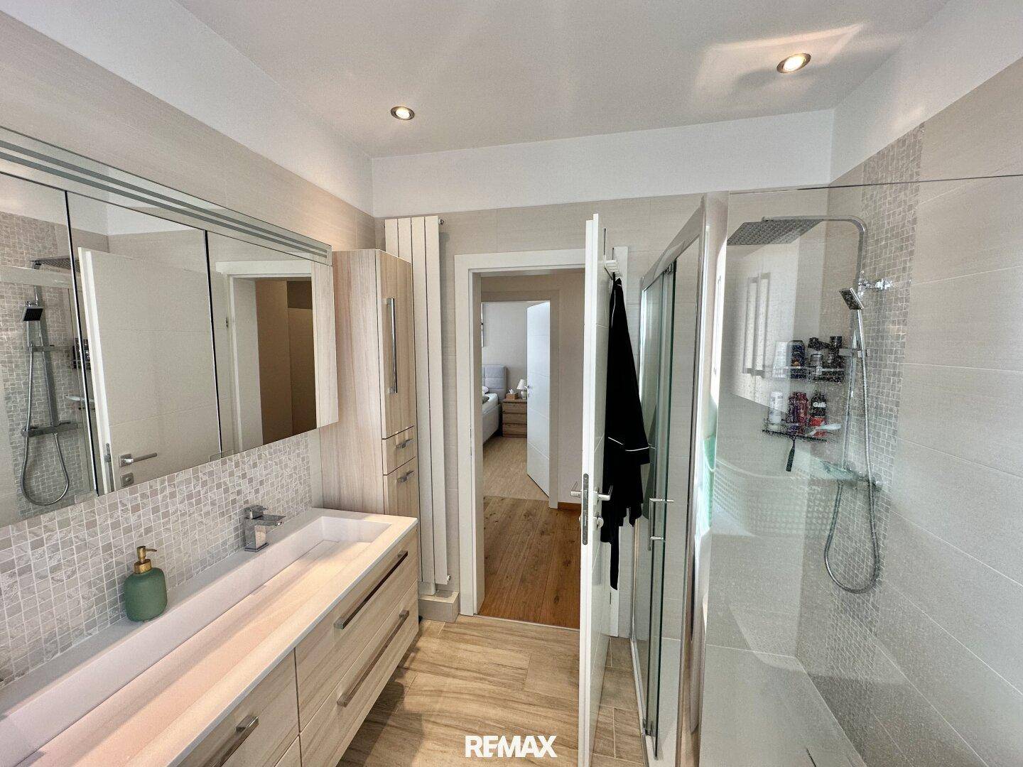 Helles Badezimmer mit großer Dusche, modernem Waschtisch und Zugang zu einem weiteren Raum.