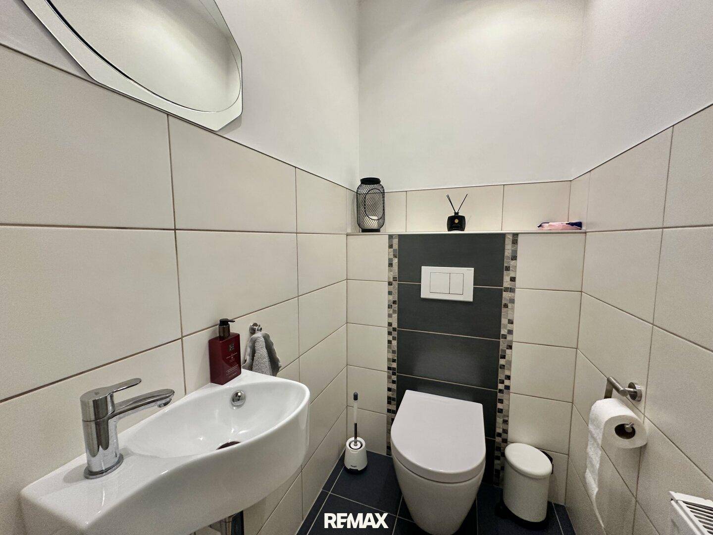 Modernes Gäste-WC mit Wand-WC, kleinem Waschbecken und stilvollen Fliesen.