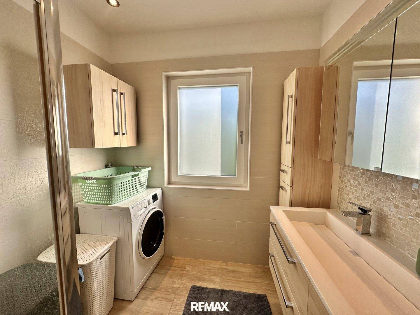 Modernes Badezimmer mit Dusche, Waschmaschine und einem Fenster für natürliche Belüftung.