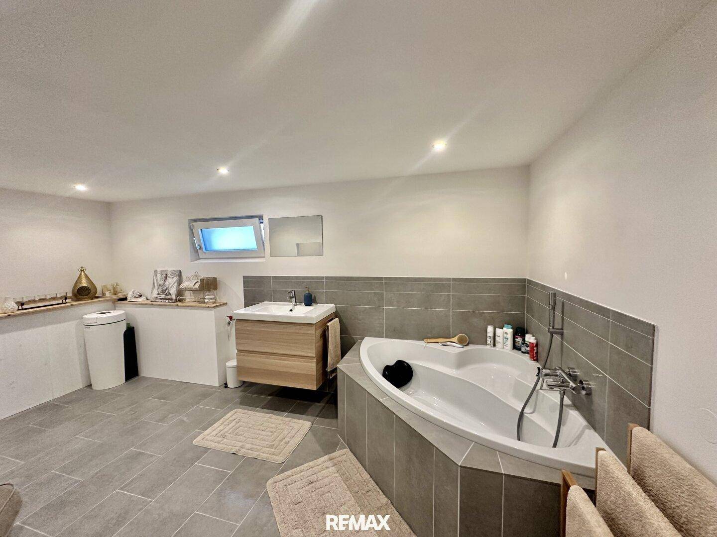 Modernes Badezimmer mit Eckbadewanne, Einzelwaschbecken und grauen Fliesen.