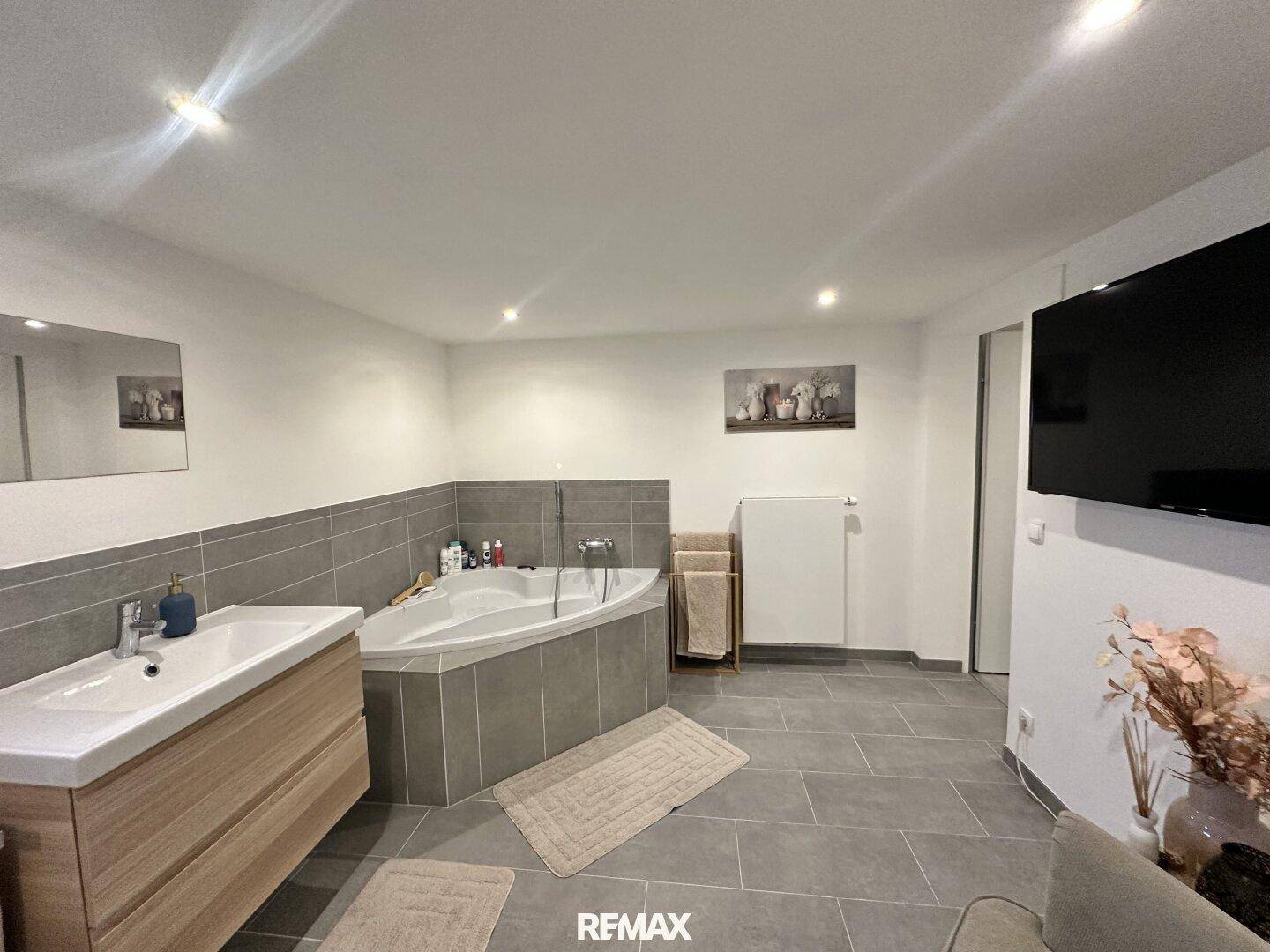 Geräumiges Badezimmer mit Eckbadewanne, modernem Waschtisch und Wandfernseher.
