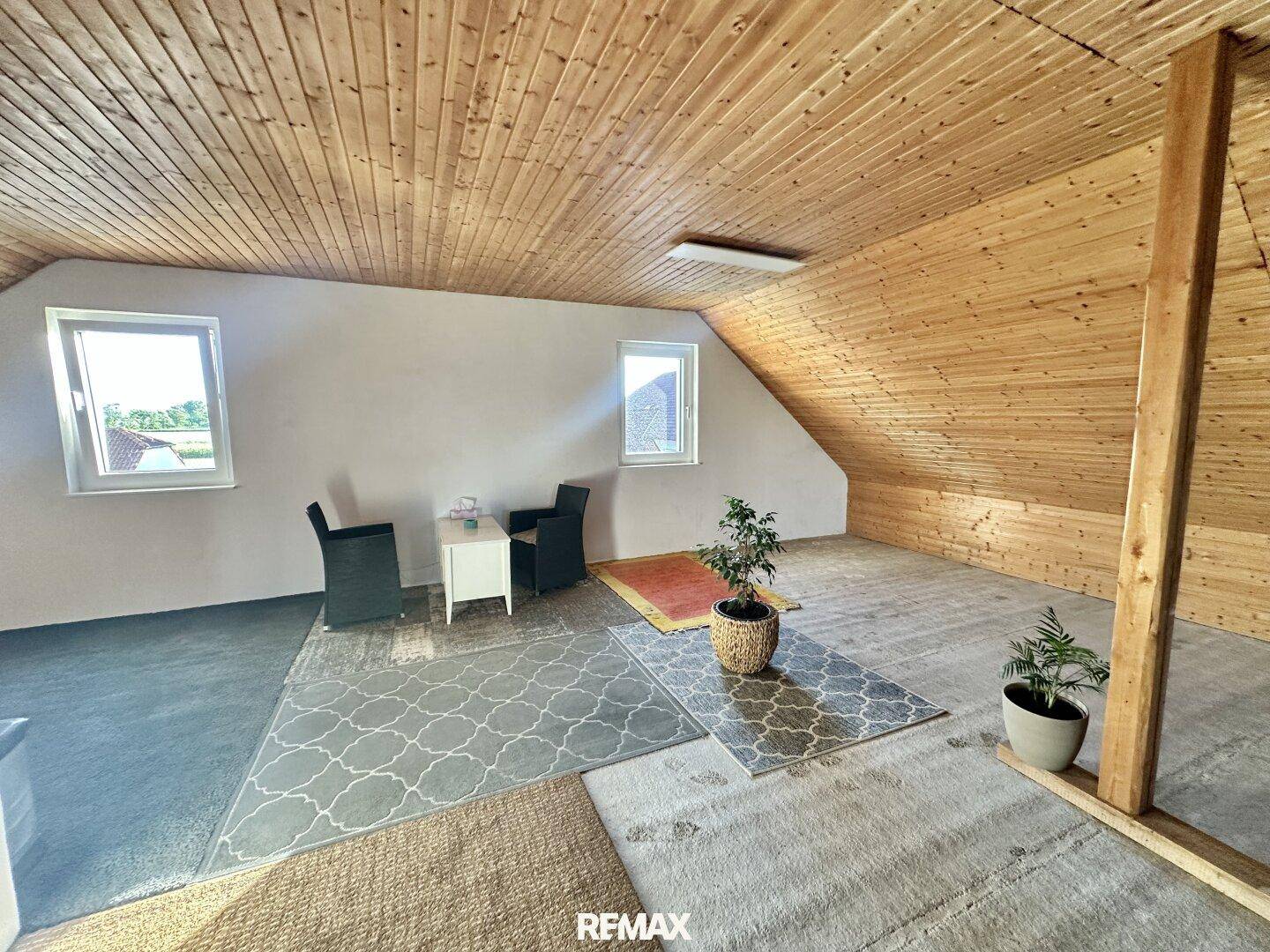 Gemütlicher Dachbodenraum mit Holzverkleidung, schrägen Wänden und Fenstern.