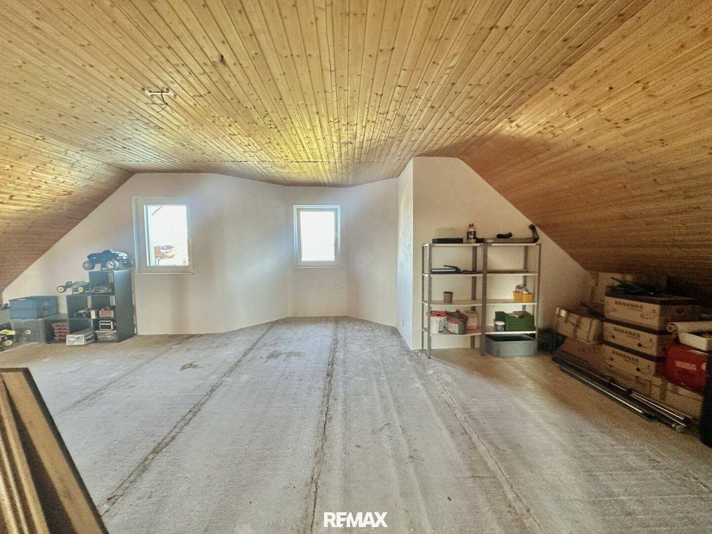 Unausgebauter Dachbodenraum mit Holzdecke und Betonboden, genutzt als Lagerfläche.