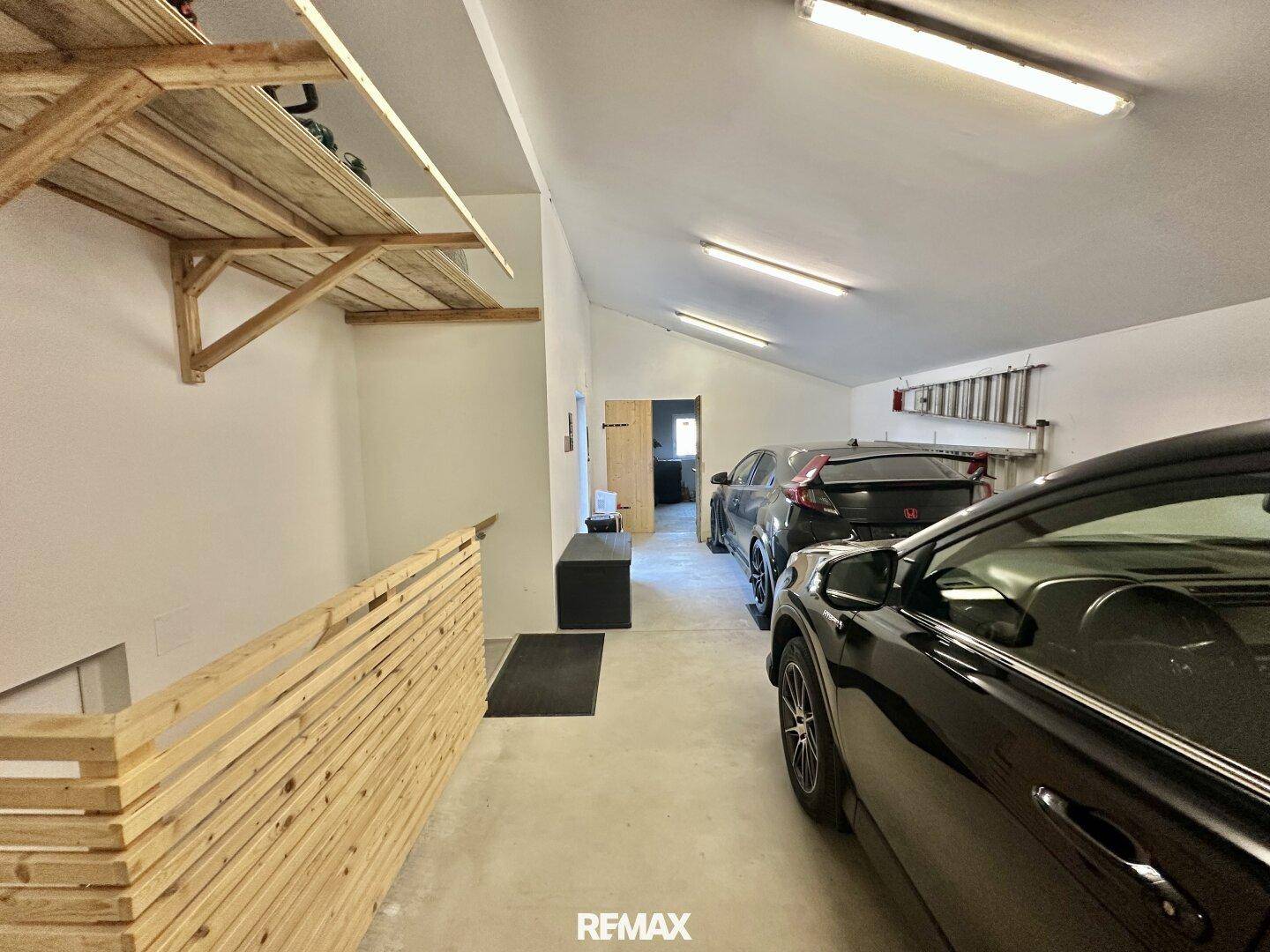 Helle Garage mit mehreren Fahrzeugen und praktischen Holzregalen.
