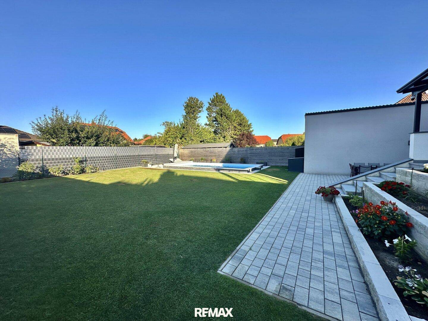 Großer Garten mit weitläufiger Rasenfläche, Pool im Hintergrund und sonniger Lage.