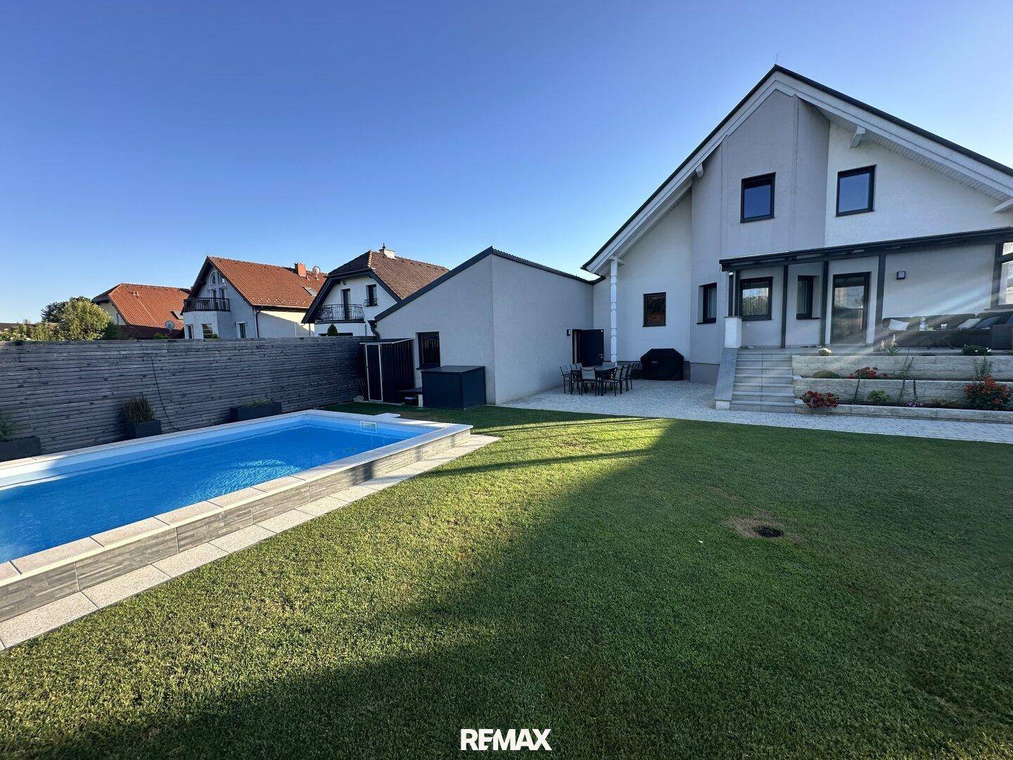Rückansicht des Hauses mit überdachter Terrasse, Pool und weitläufigem Gartenbereich.