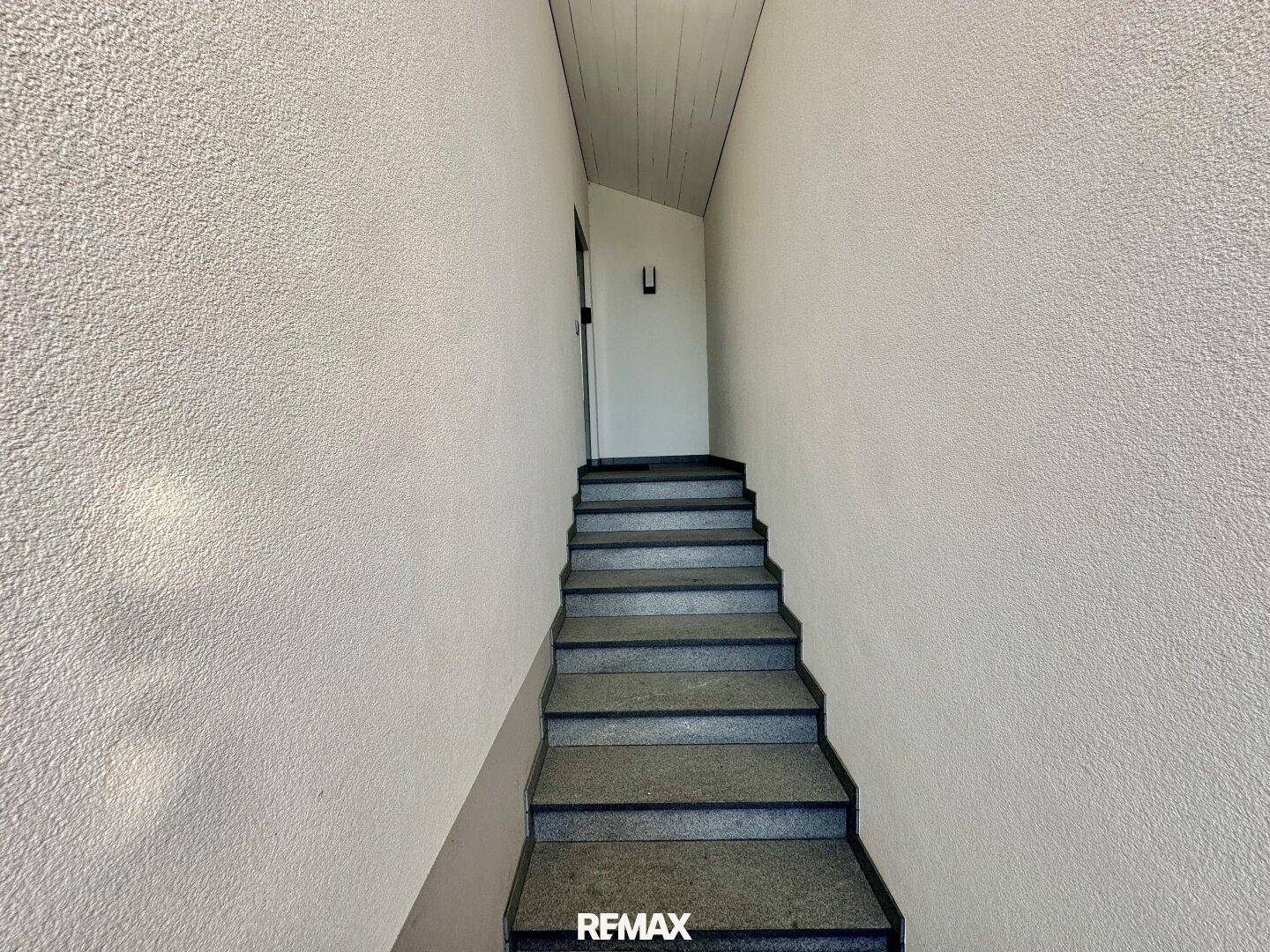Treppenaufgang mit grauen Stufen und schlichten weißen Wänden, führt in die obere Etage.