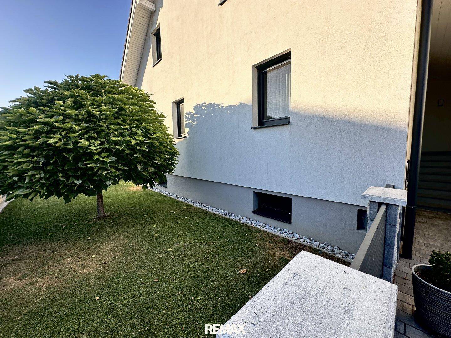 Seitenansicht des Hauses mit einem kleinen Baum und einem Kiesstreifen entlang des Sockels.