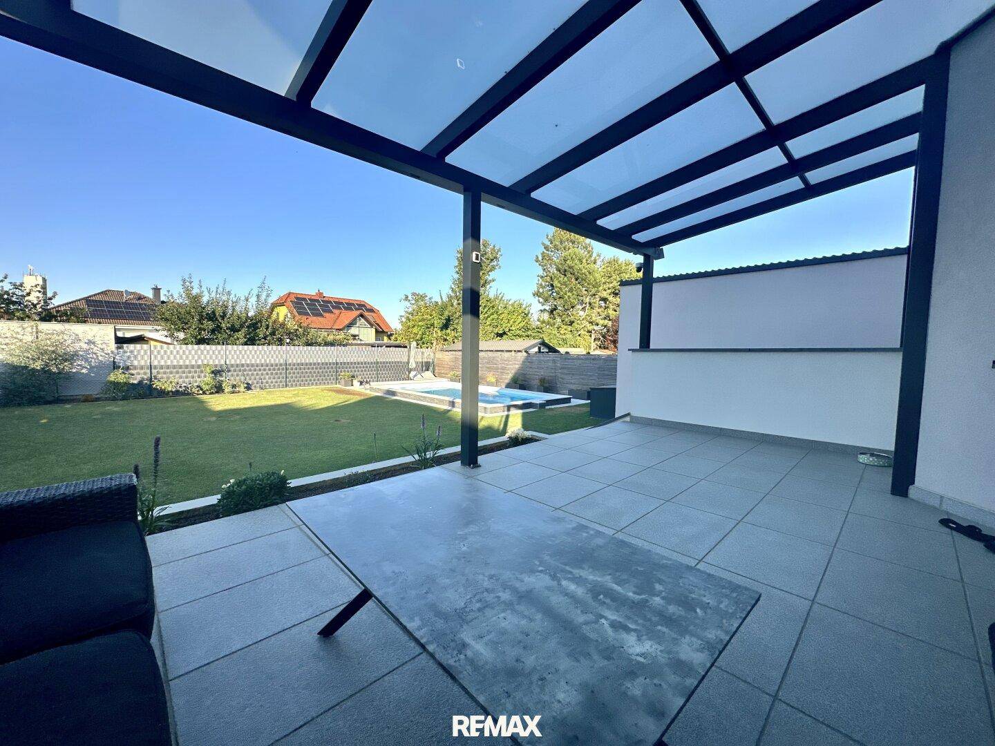 Geräumige überdachte Terrasse mit Fliesenboden, Blick auf den Garten und den Swimmingpool.