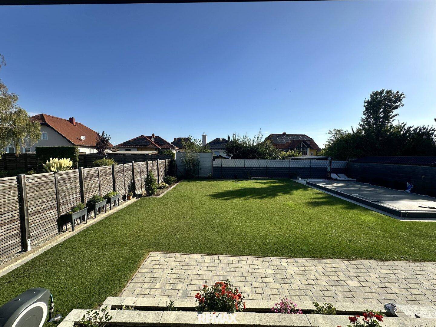 Weitläufiger Blick von der Terrasse auf den grünen Garten und den abgedeckten Poolbereich.