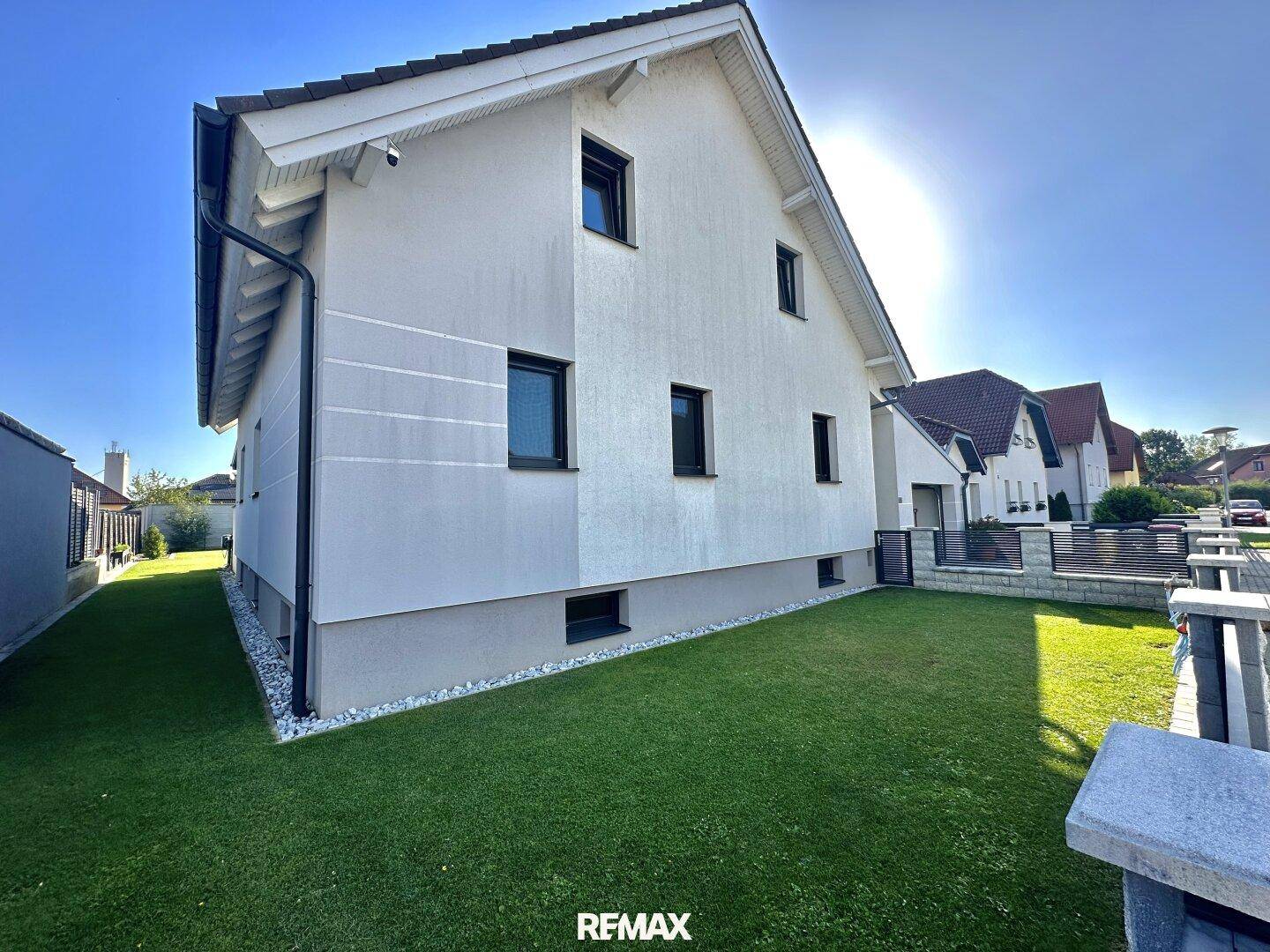 Seitenansicht des Hauses mit gepflegtem Rasen, Zaun und klarer architektonischer Linie.