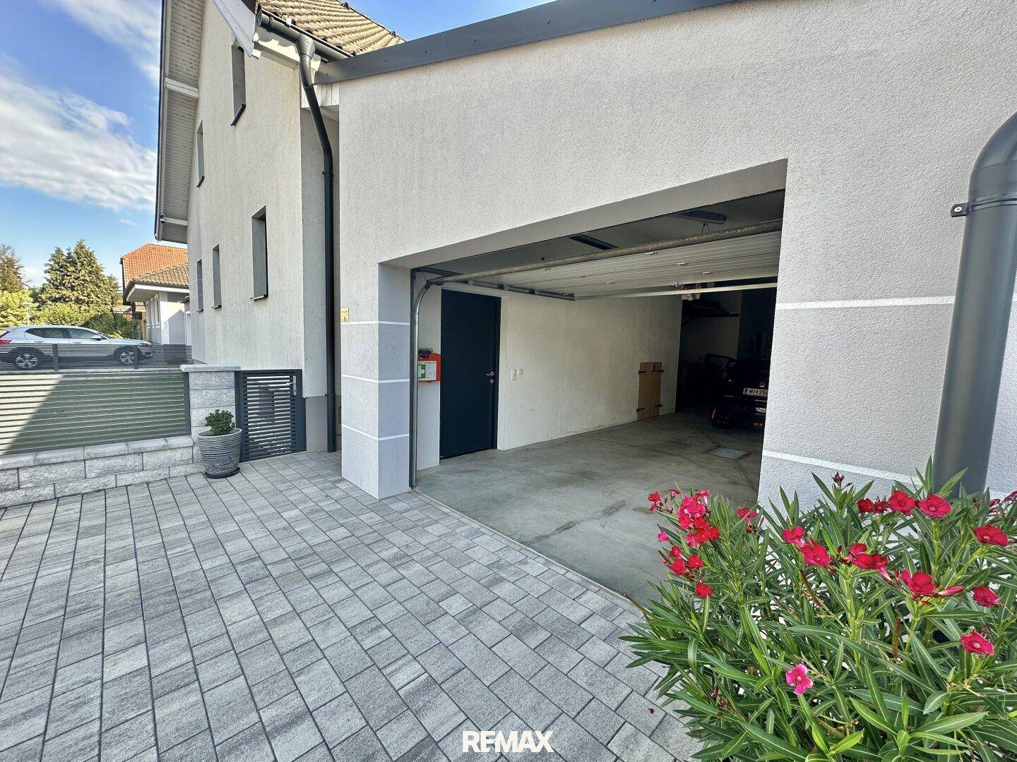 Offene Garage mit gepflastertem Vorplatz und direktem Zugang zum Haus.