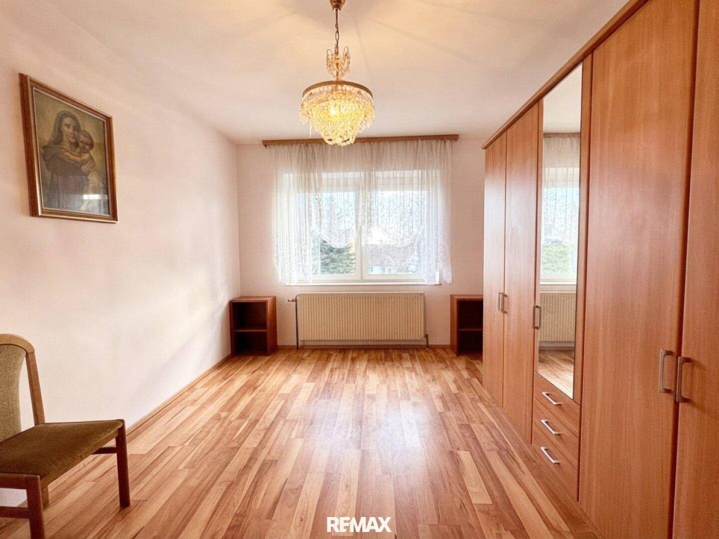 Helles Schlafzimmer mit Holzboden, großem Kleiderschrank und Fenster für natürliches Licht.